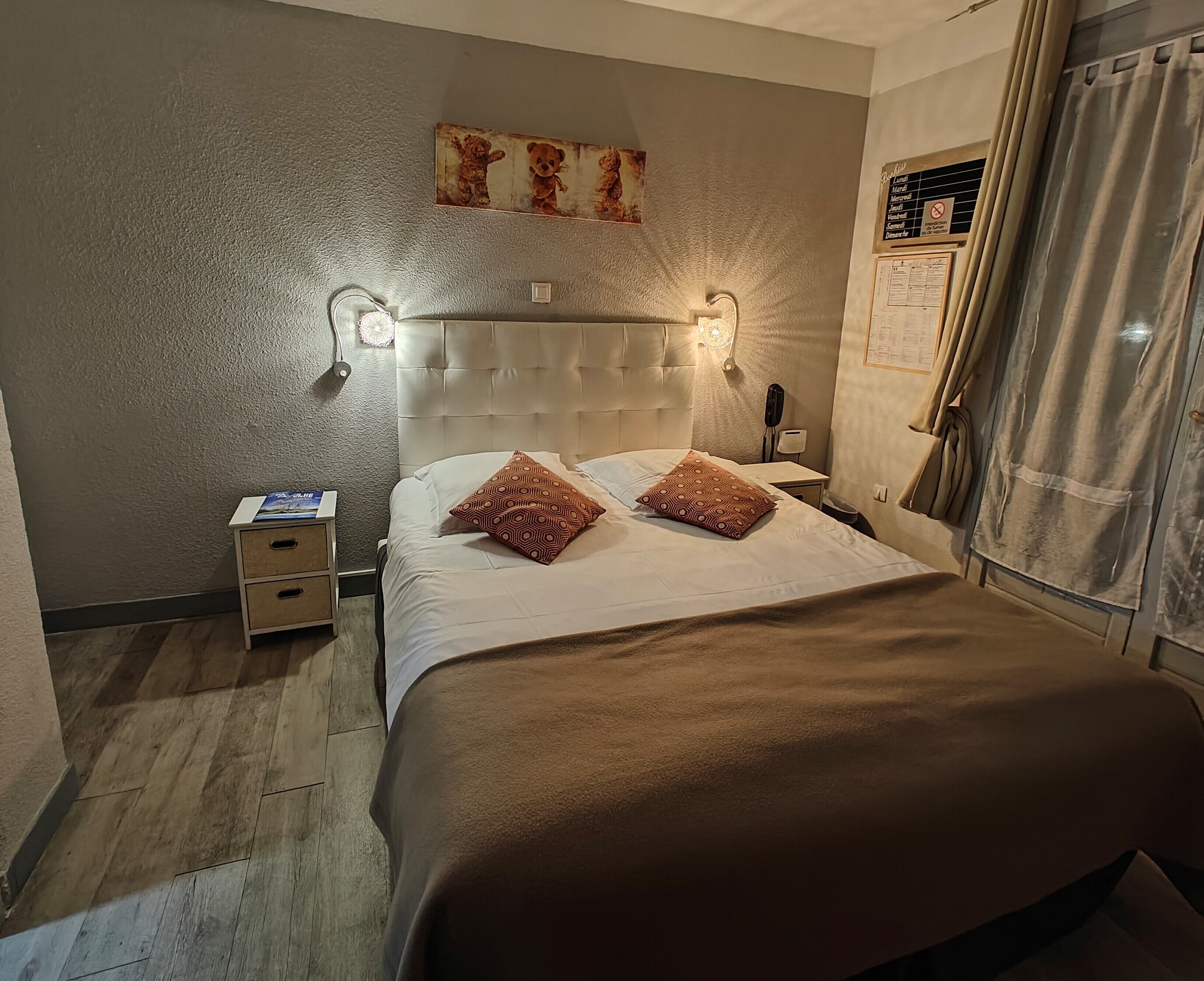Een keurig opgemaakt slaapkamer met een bed, twee gestreepte kussens, een nachtkastje met een lamp en een klein nachtkastje.