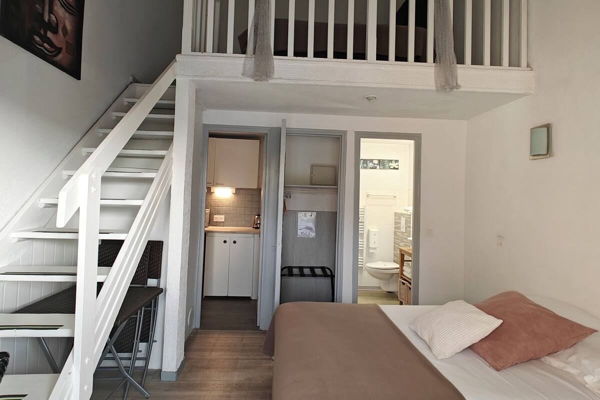 A bedroom with a bed, a staircase, and a kitchen area.