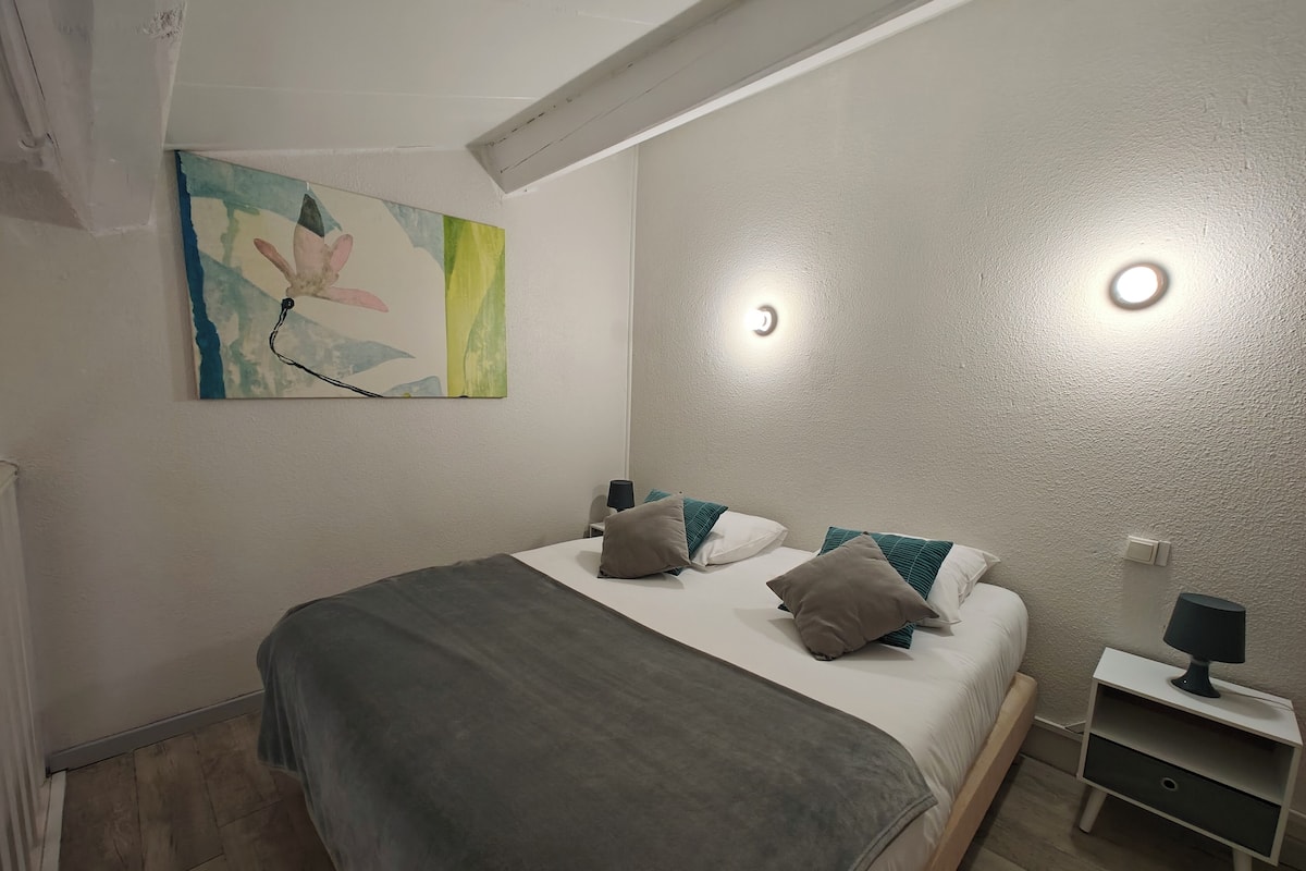 A modern bedroom with a bed, pillows, a nightstand, and a wall-mounted light fixture.