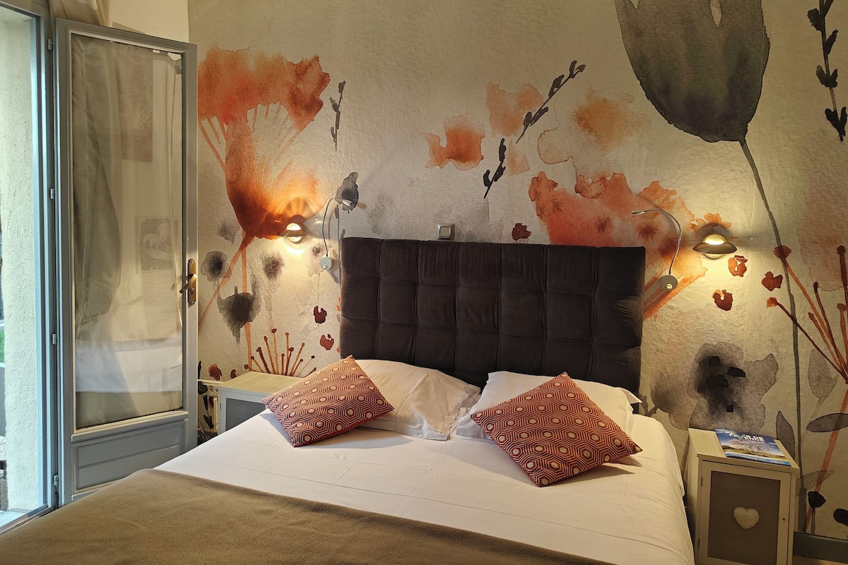 A hotel room with a large bed, two patterned pillows, a headboard, and a wall with a floral mural.