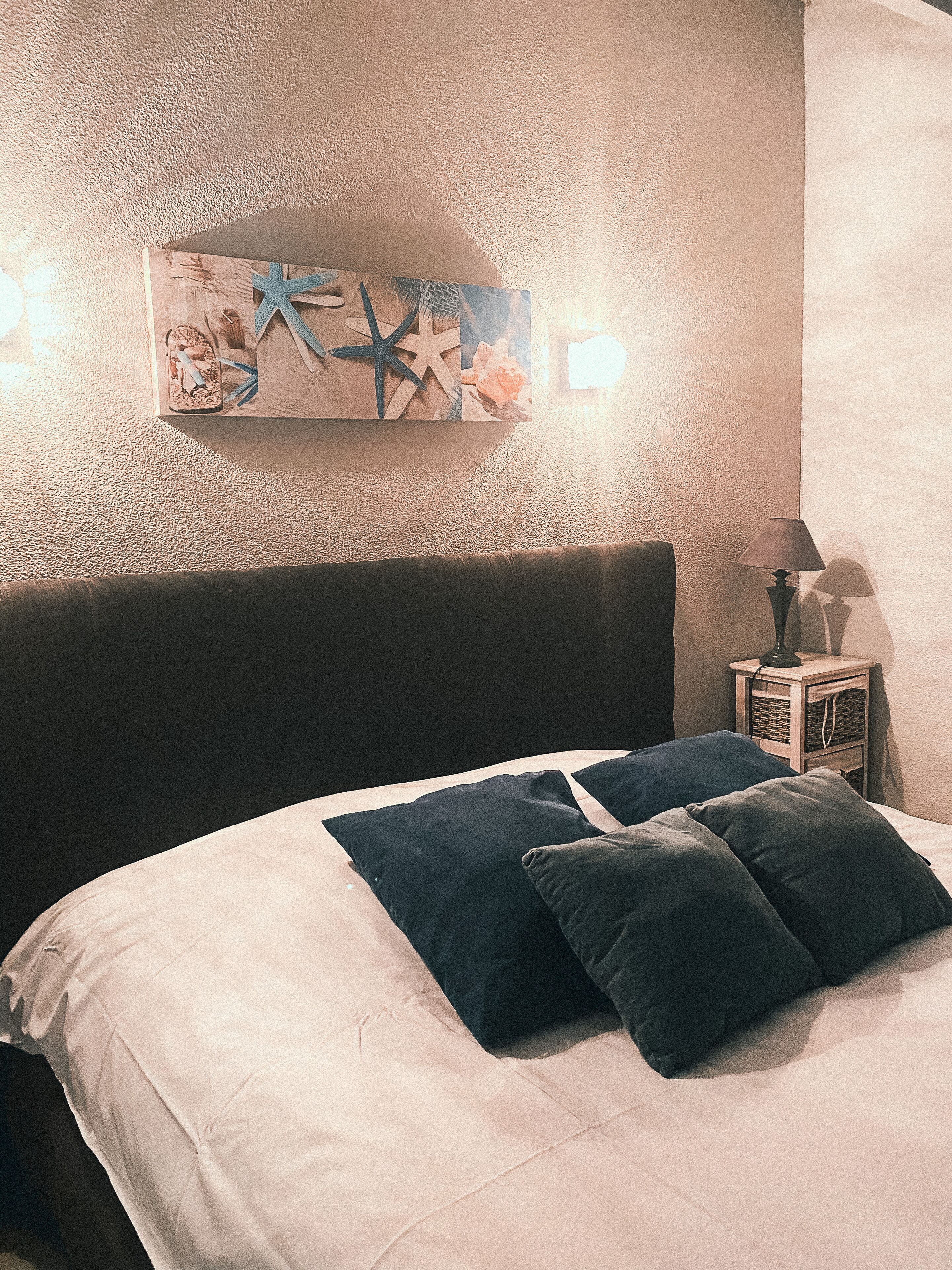 A bedroom with a bed, pillows, a nightstand, a lamp, and a wall art piece.