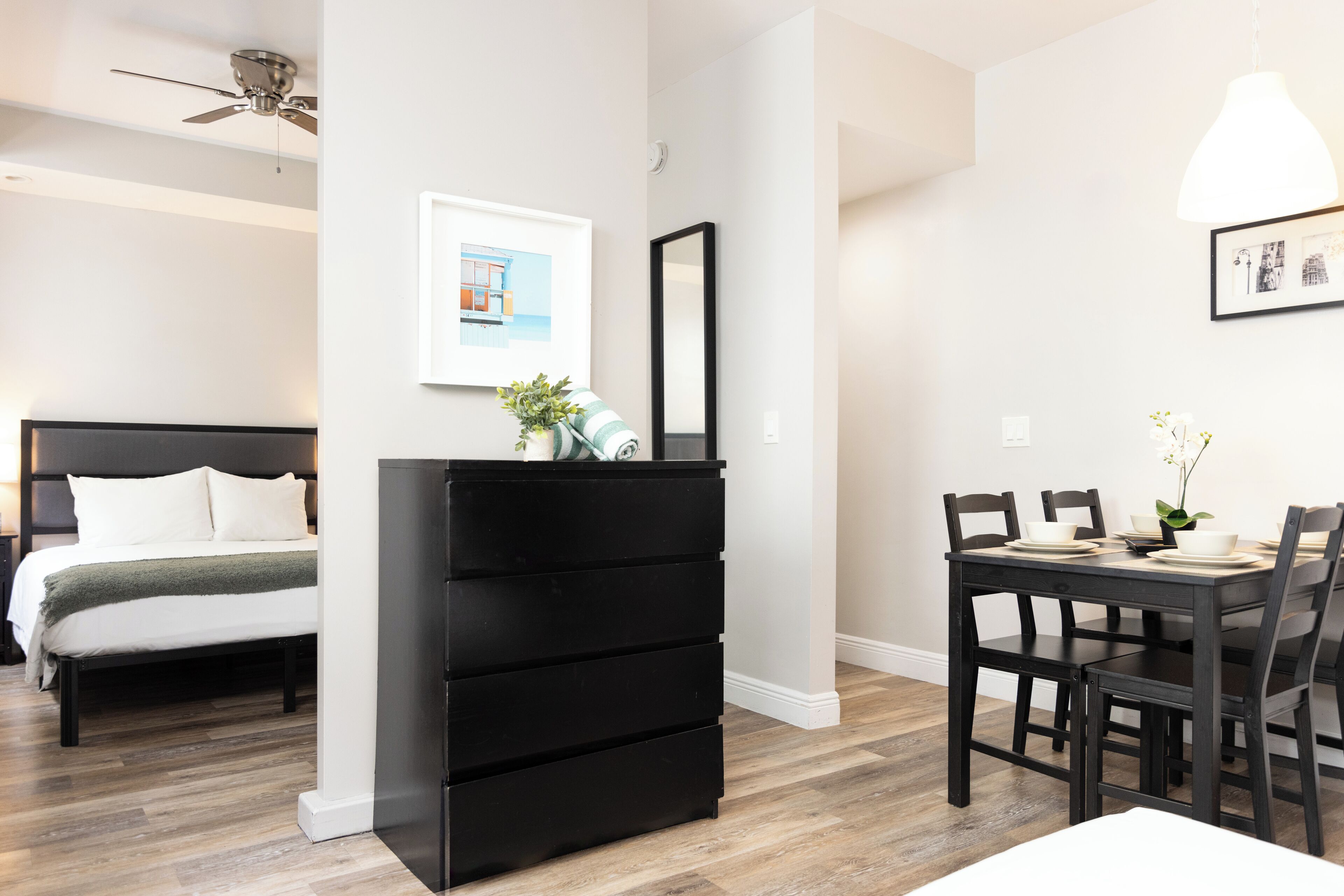 A bedroom with a bed, a dresser, a desk with chairs, and a ceiling fan.