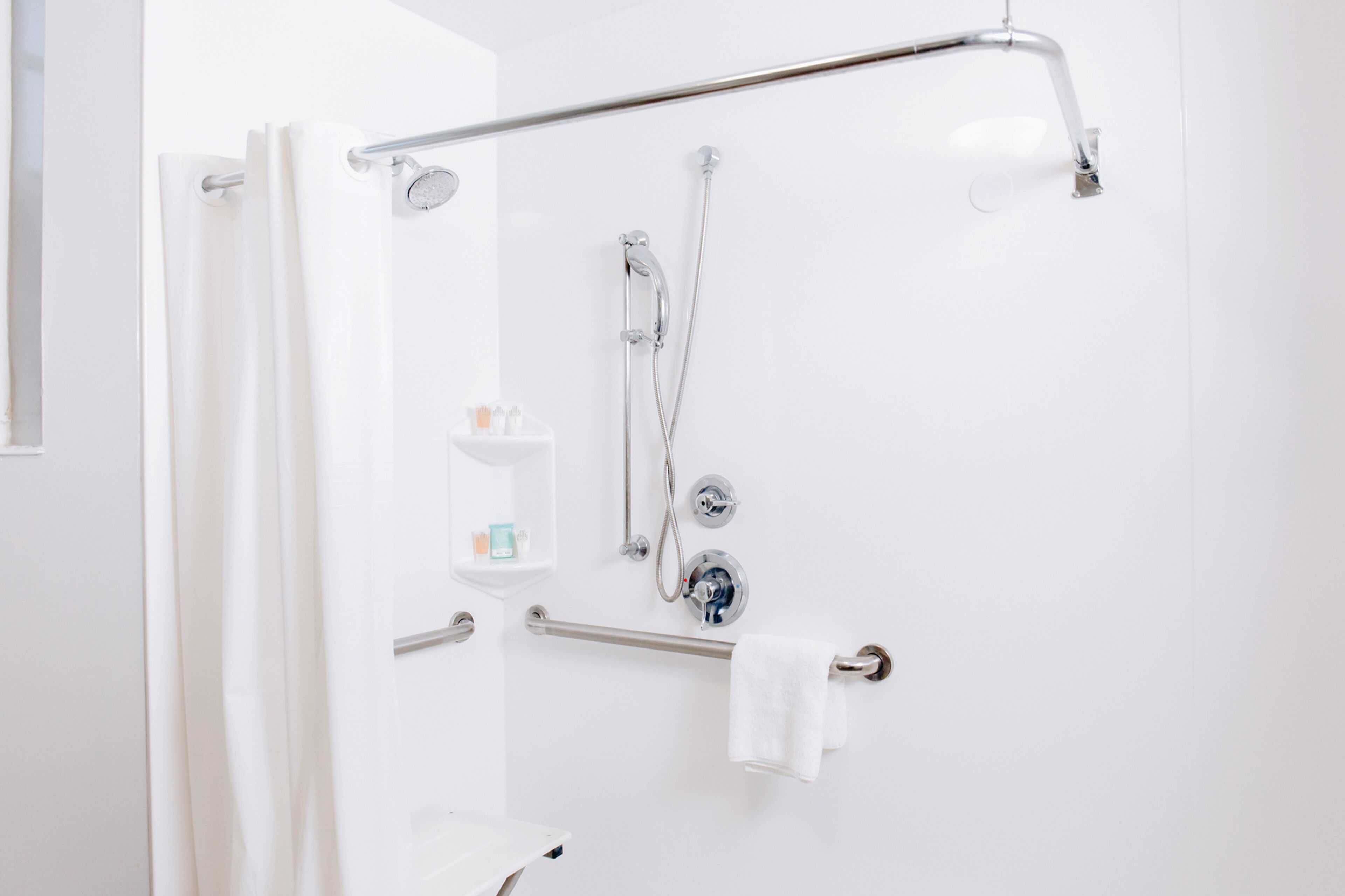 Un baño con ducha, barra de apoyo y toallero.
