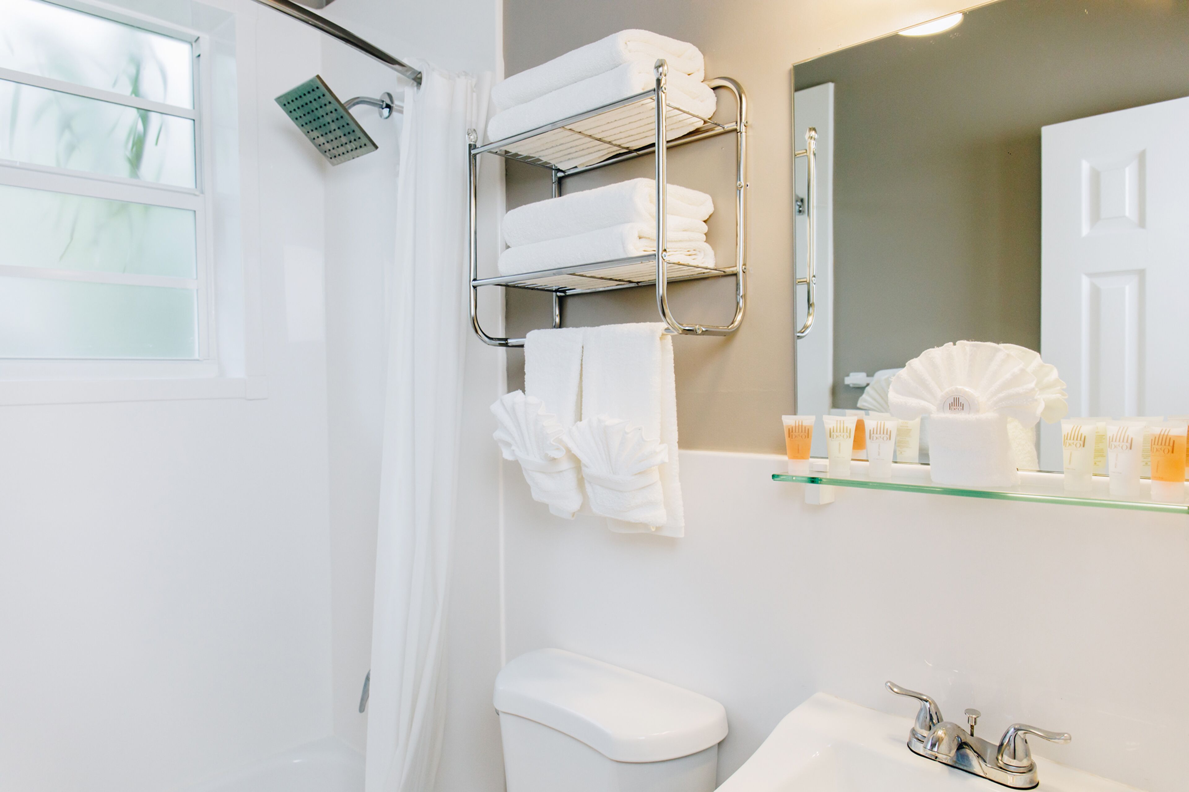 A bathroom with a shower, a toilet, a sink, and a towel rack with folded towels.