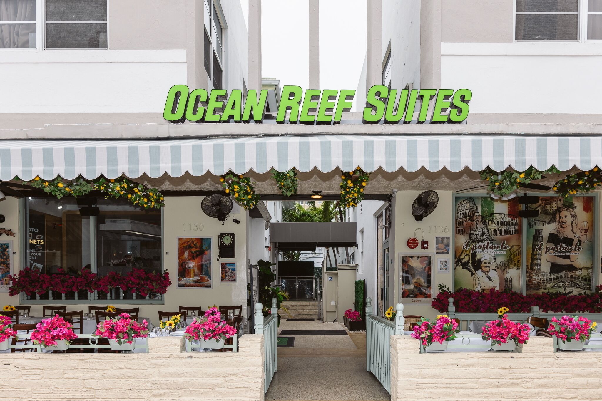 Das Außere von Ocean Reef Suites mit gestreifter Markise, Blumenarrangements und einem Schild über dem Eingang.