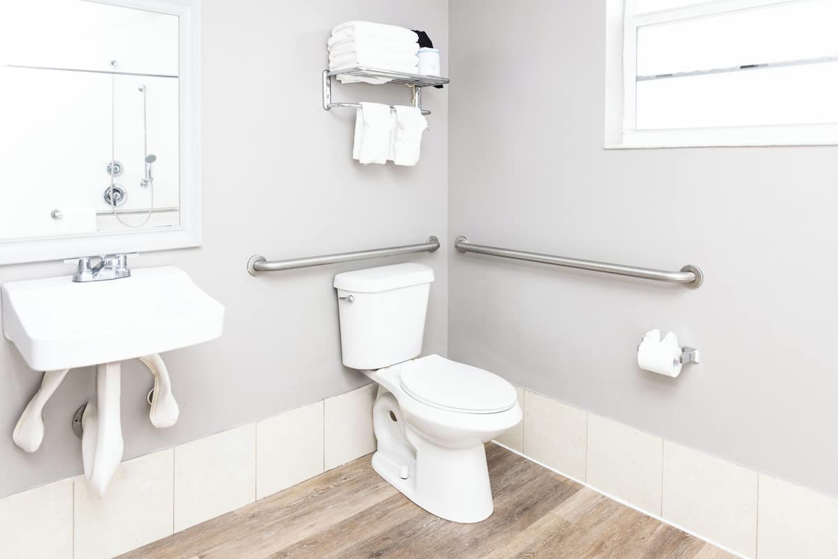 A modern bathroom with a white sink, toilet, and grab bars.