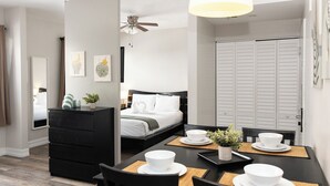 Ein modernes Hotelzimmer mit einer ordentlich eingerichteten Essecke, einem Bett mit weißem Kopfteil und einem Kleiderschrank.