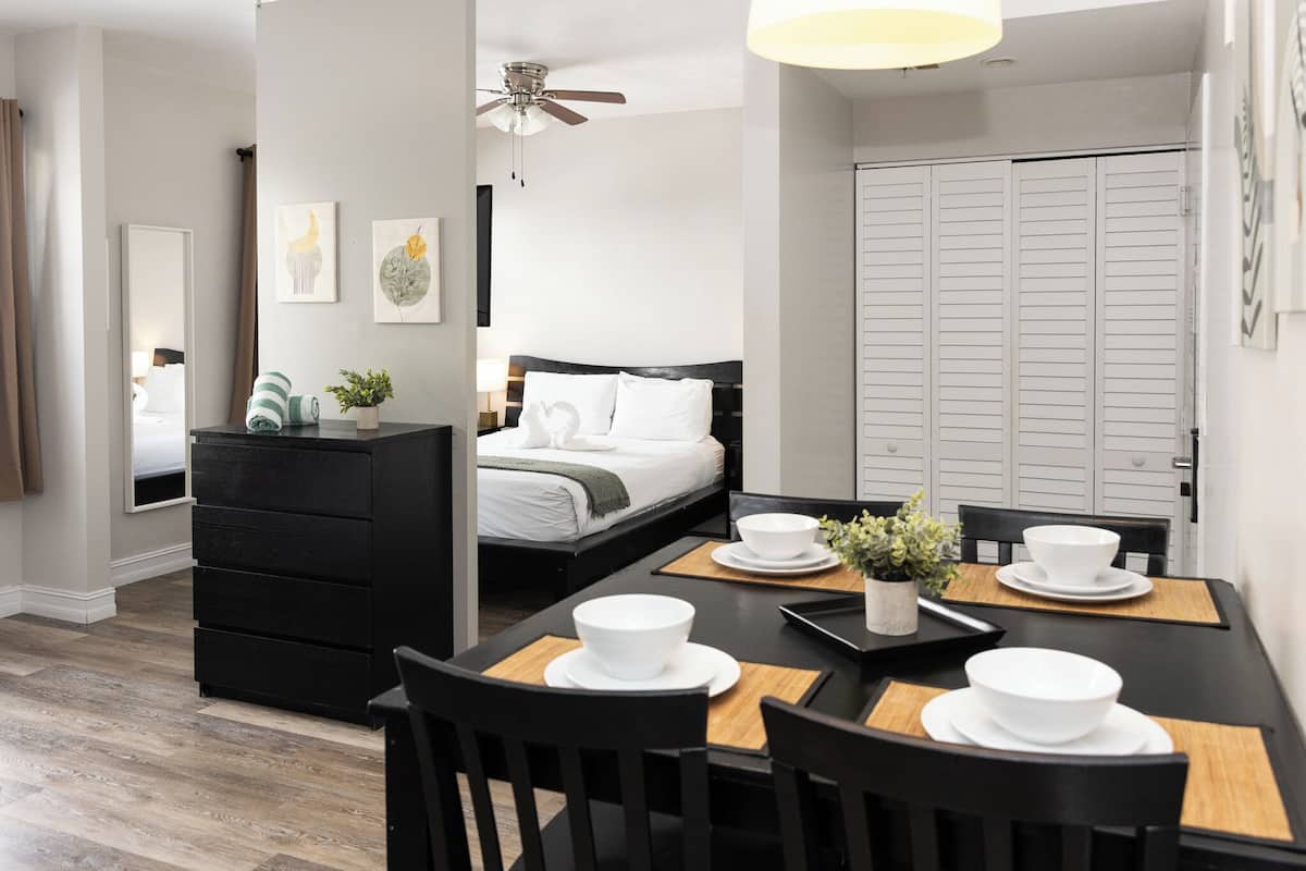 A modern hotel room with a neatly arranged dining area, a bed with a white headboard, and a wardrobe.