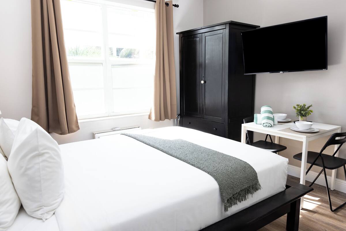 A hotel room with a bed, a desk, a television, and a wardrobe.