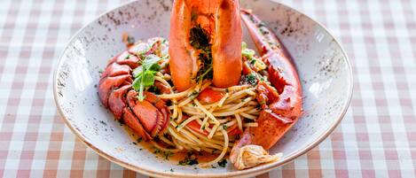 A plate of spaghetti with lobster tail and vegetables on a checkered tablecloth.