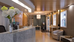 Eine moderne Hotellobby mit einem Marmor-Rezeptionsschalter, einer Kristallleuchter und einer Sitzecke mit einem weißen Sessel und einem kleinen Tisch mit einem Korb.