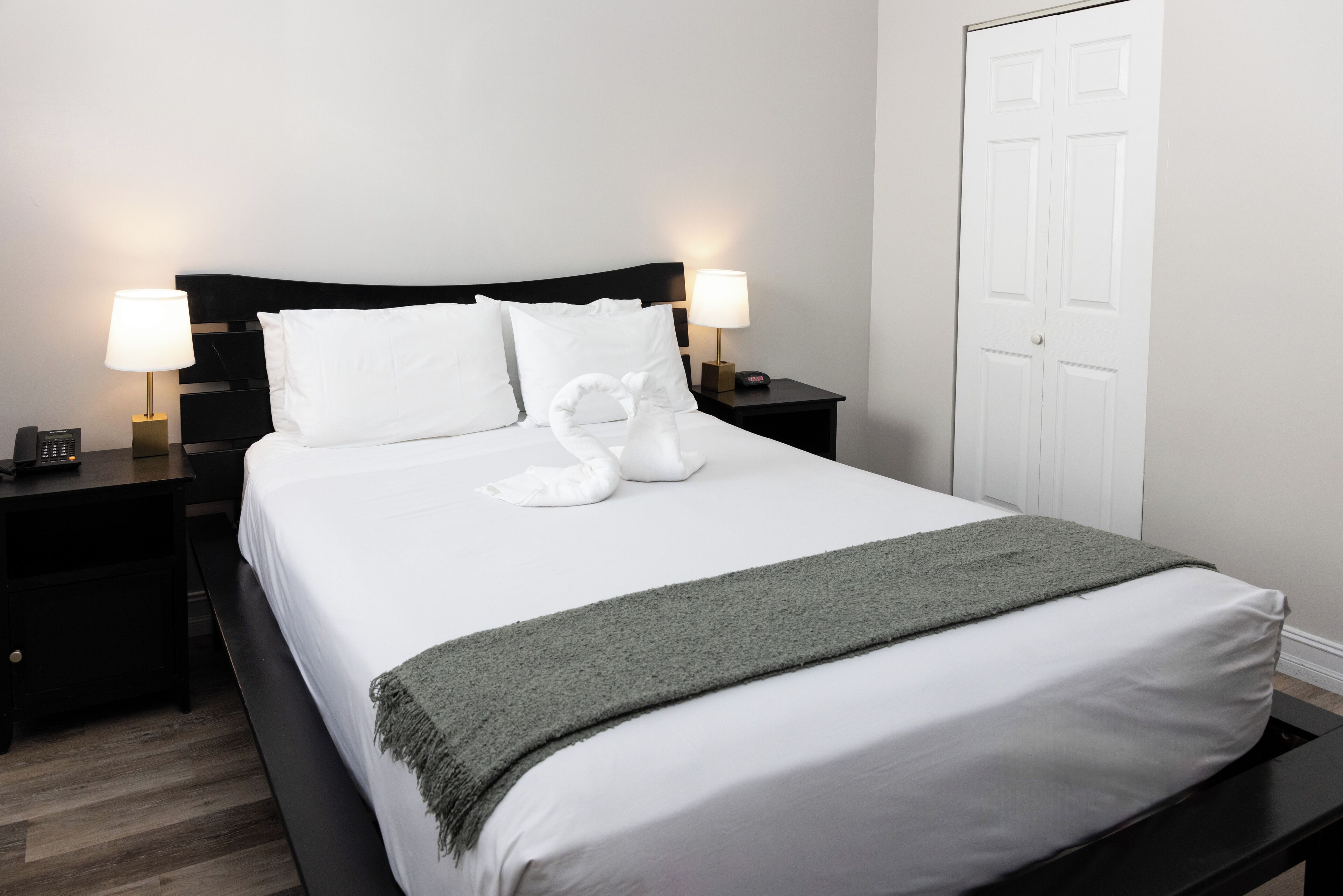 A neatly made bed with white linens, two bedside lamps, and a grey throw blanket.