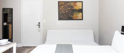 Hotellihuone, jossa on sänky, työpöytä, tuoli, valkoinen ovi ja taulu seinällä.
