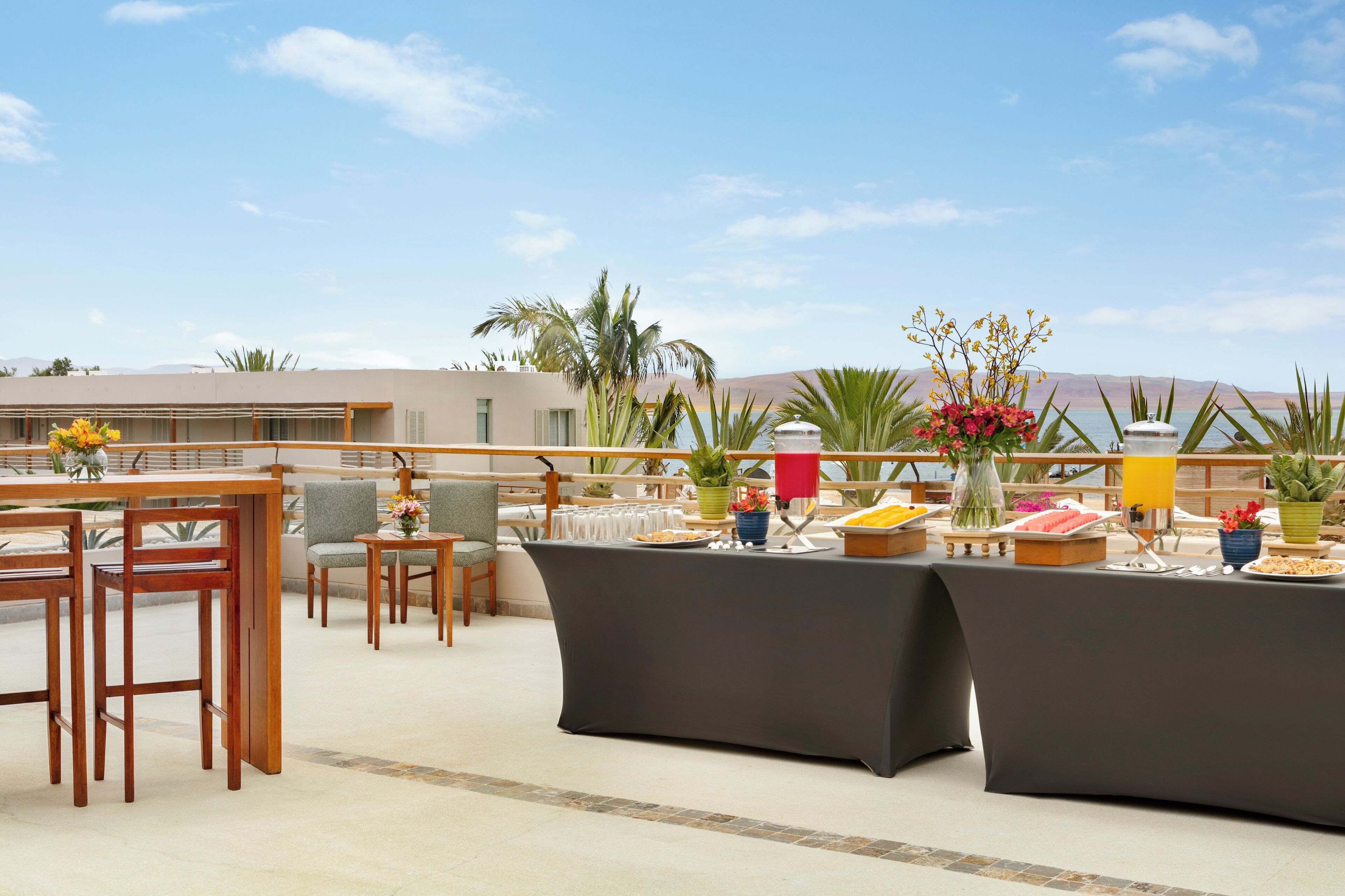 Un área de comedor en la azotea con barra libre, mesas al aire libre y vistas a las montañas.