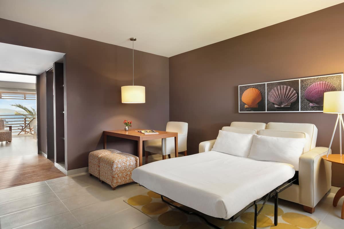 A modern hotel room with a bed, a desk, a chair, and a view of the outdoors.