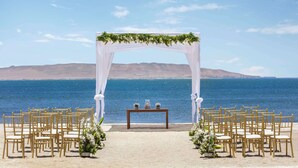 Ein Strandhochzeitsaufbau mit einem weißen Bogen und Stühlen.