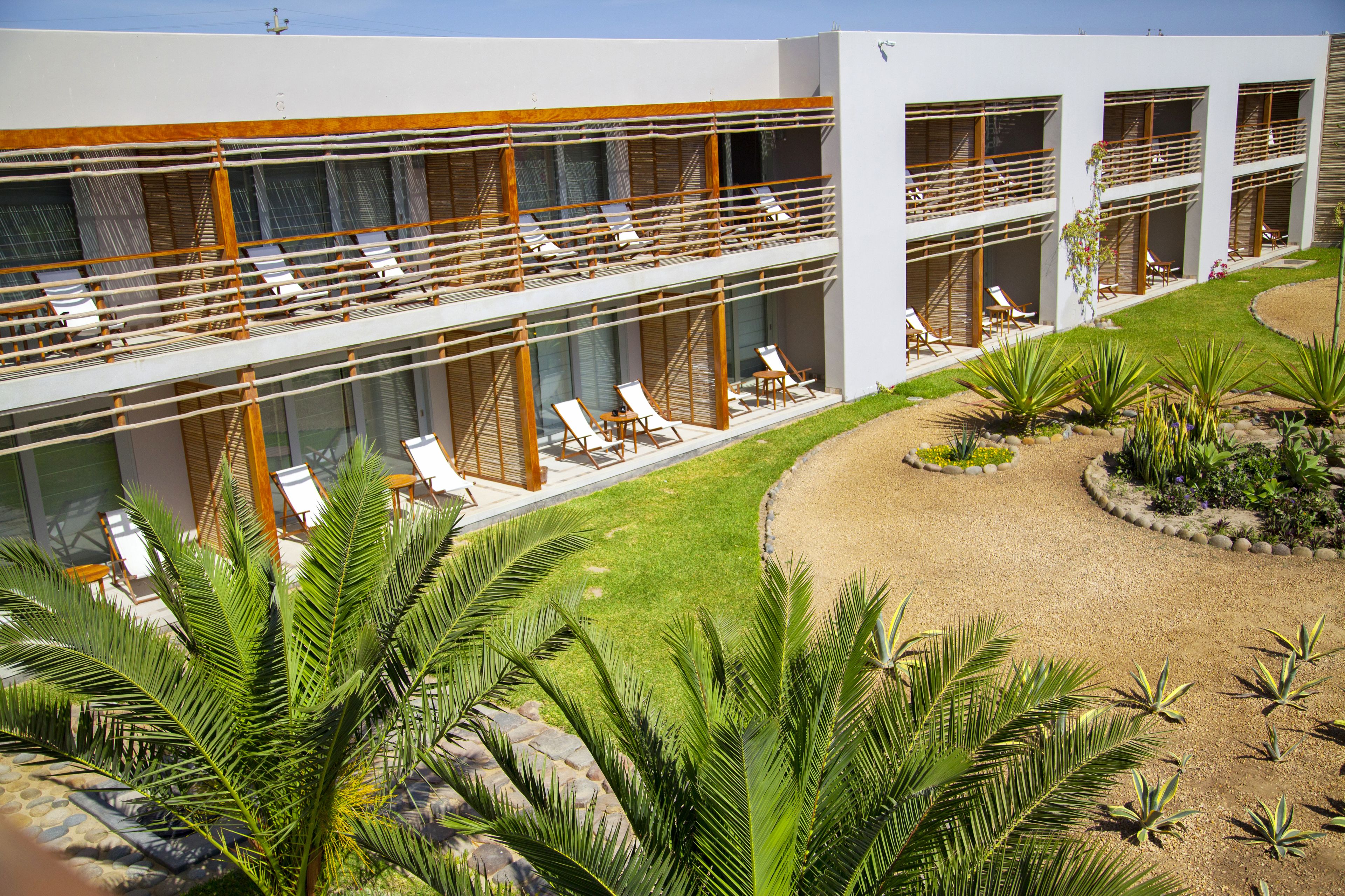 A modern hotel with multiple balconies, sun loungers, and a well-maintained garden.