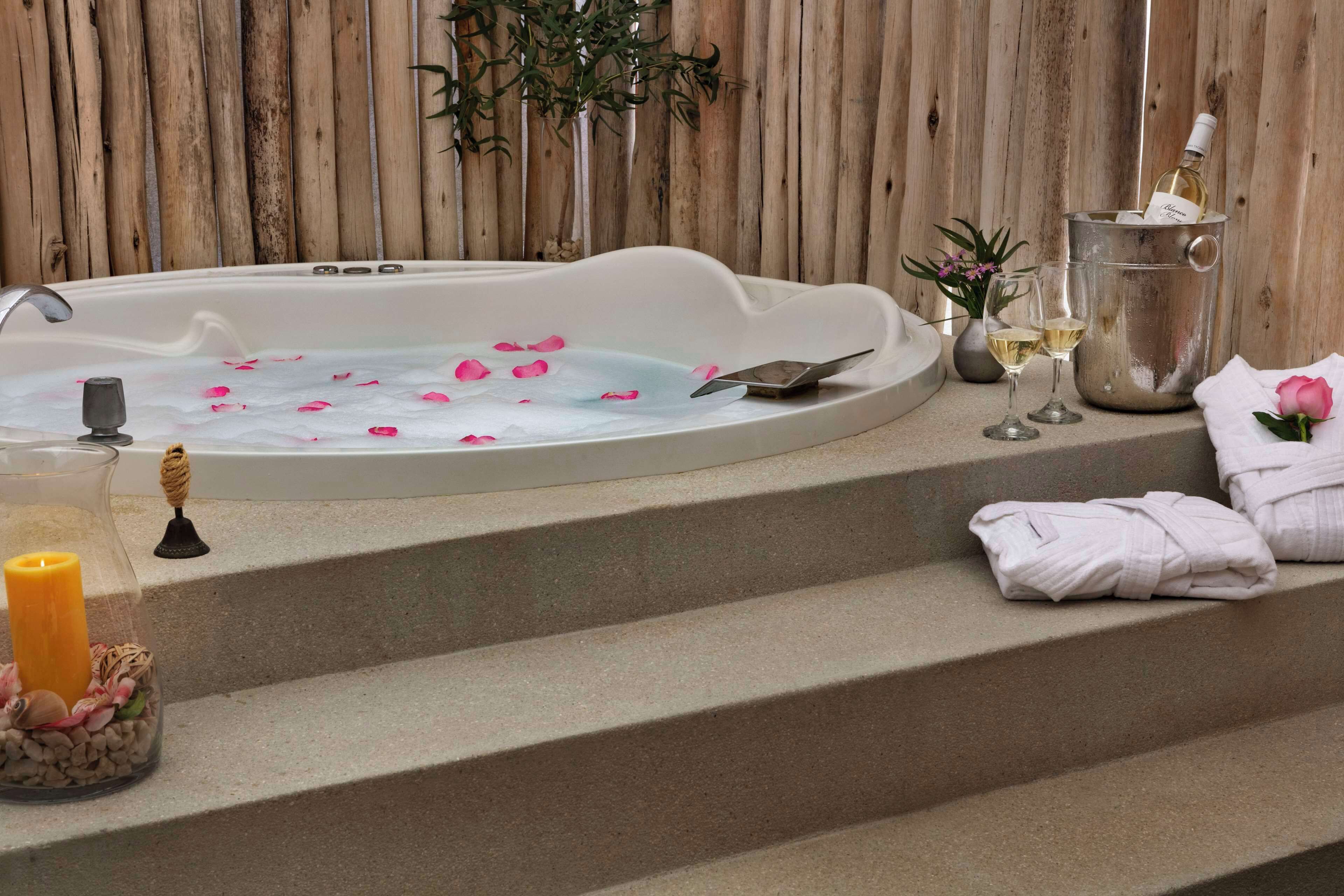 A spa area with a hot tub, steps leading up to it, a candle, a glass of wine, and towels.