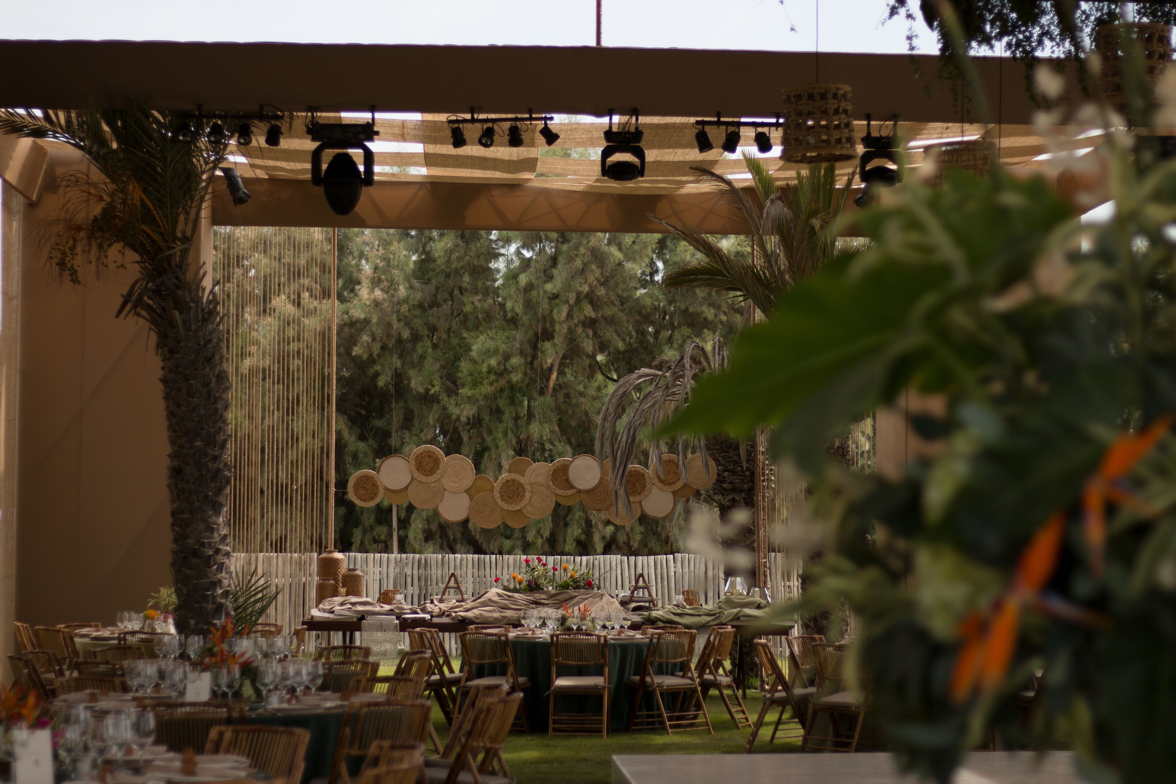 An outdoor dining area with tables set for guests, surrounded by greenery and a decorative fence.