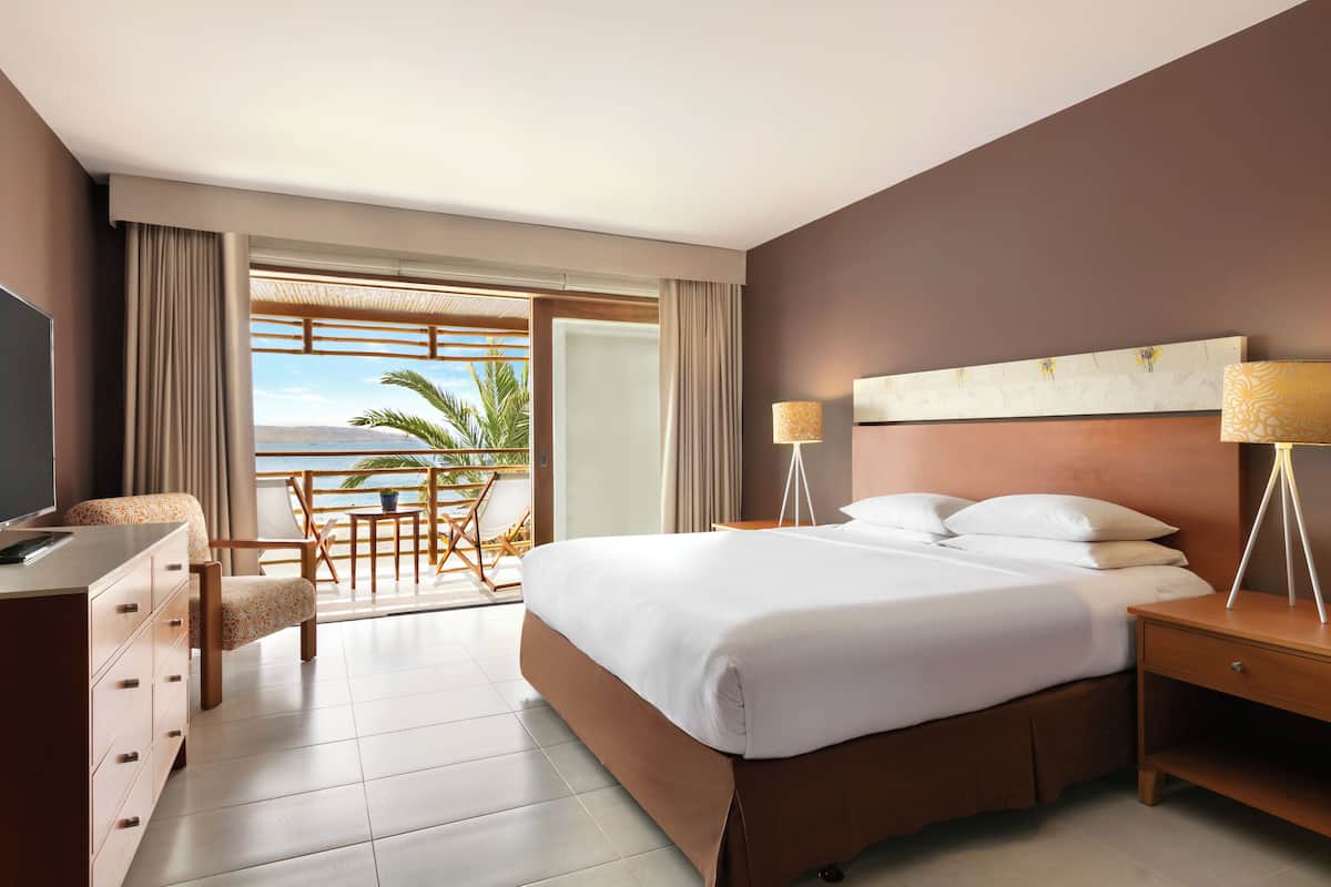 A hotel room with a bed, a desk, a chair, a lamp, and a view of the outdoors.