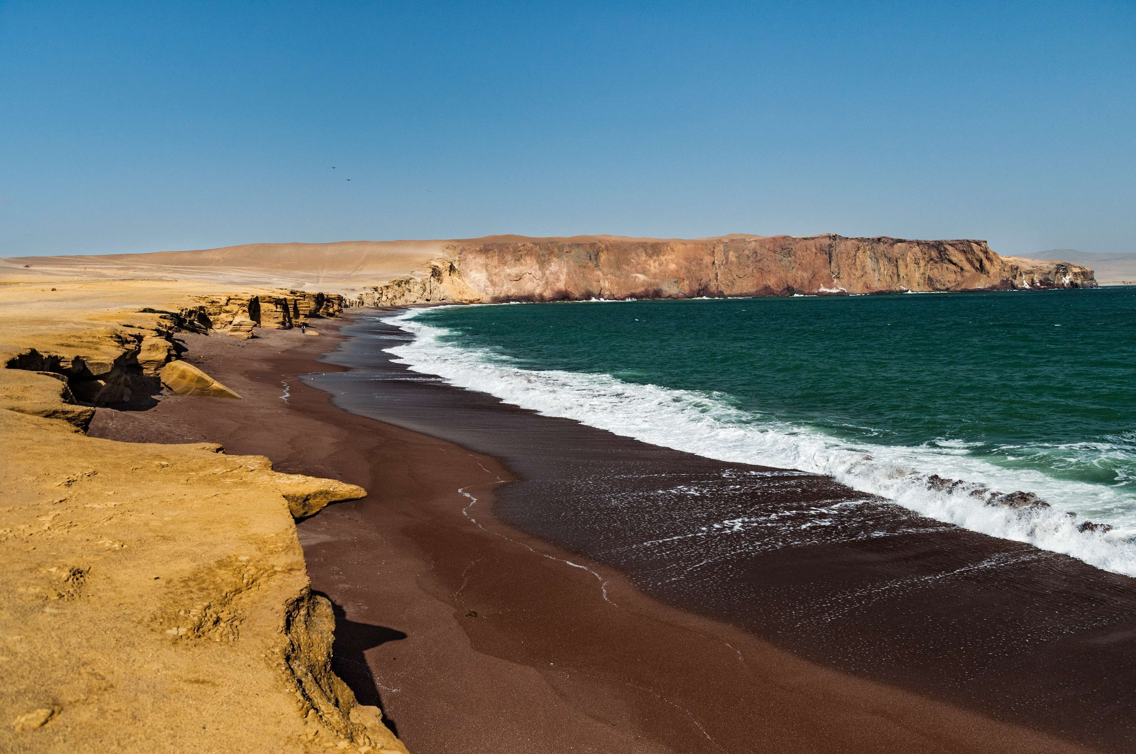 Un paisaje costero con una playa de arena, acantilados rocosos y un cielo azul despejado.
