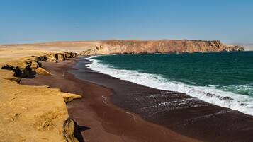 Un paisaje costero con una playa de arena, acantilados rocosos y un cielo azul despejado.