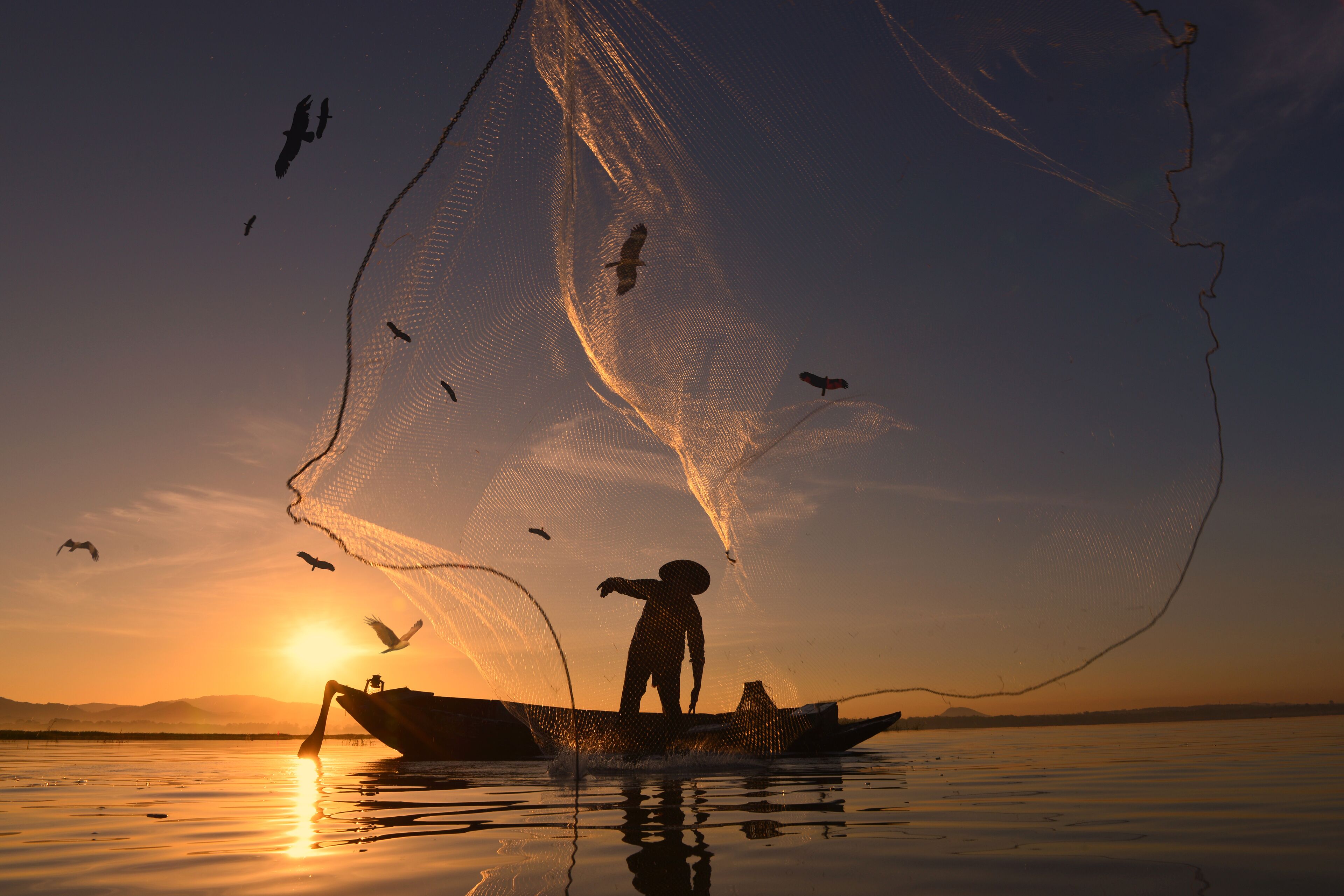 Un barco de pesca al atardecer con una persona de pie, rodeada de una red de pesca.