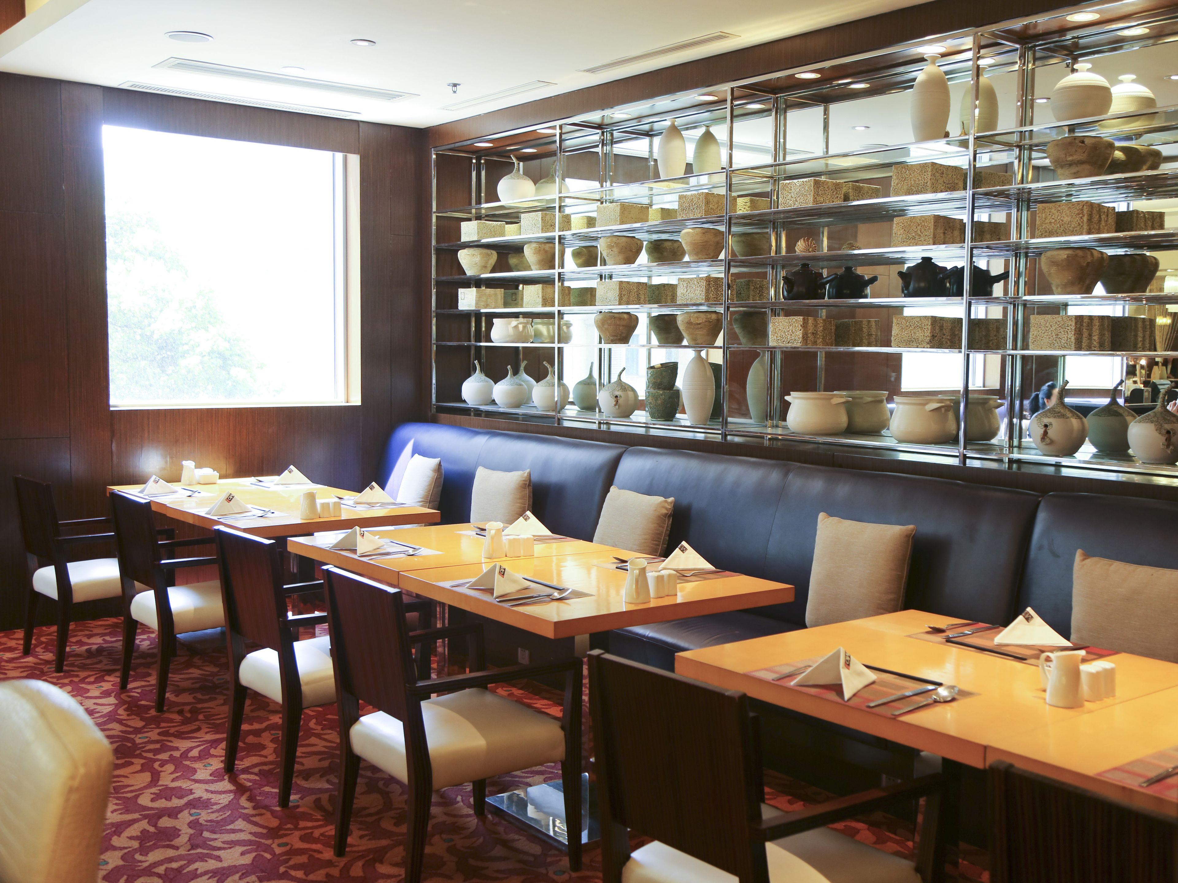 A restaurant with a glass display of pottery and a seating area with tables and chairs.