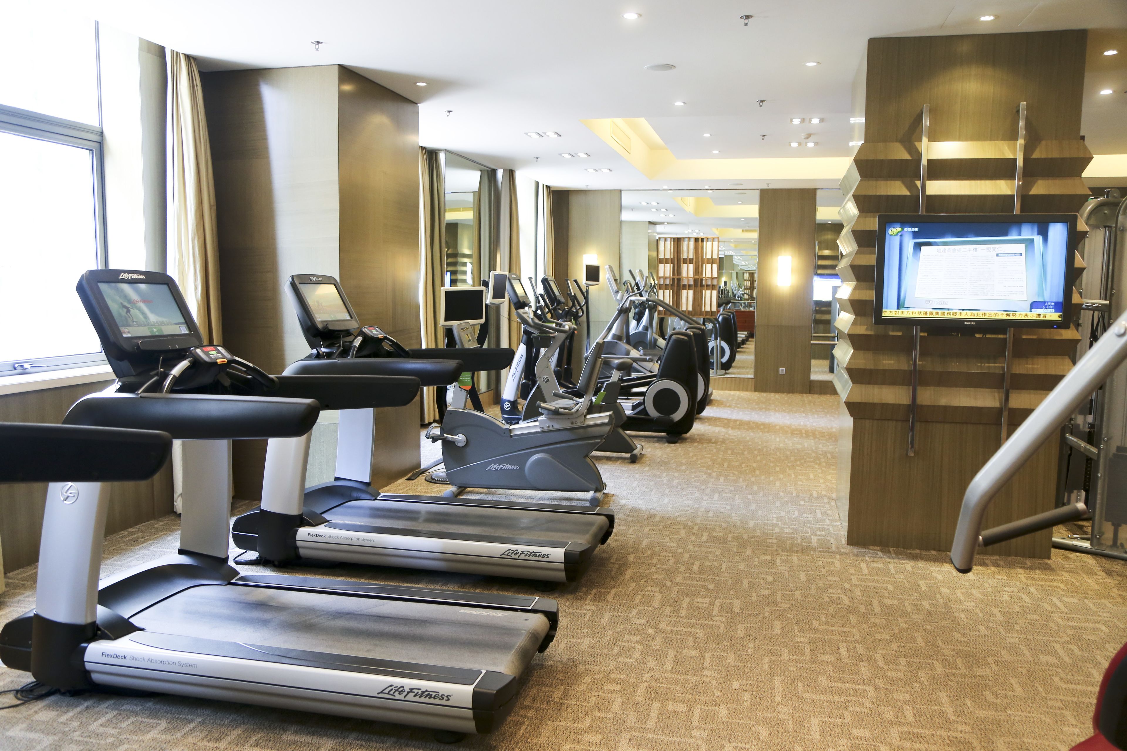 Un gimnasio con cintas de correr, elípticas y una pantalla de televisión.