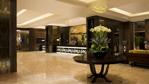 Un vestíbulo amplio con piso de mármol, una mesa redonda con un centro de flores y un espejo grande que refleja la estancia.
