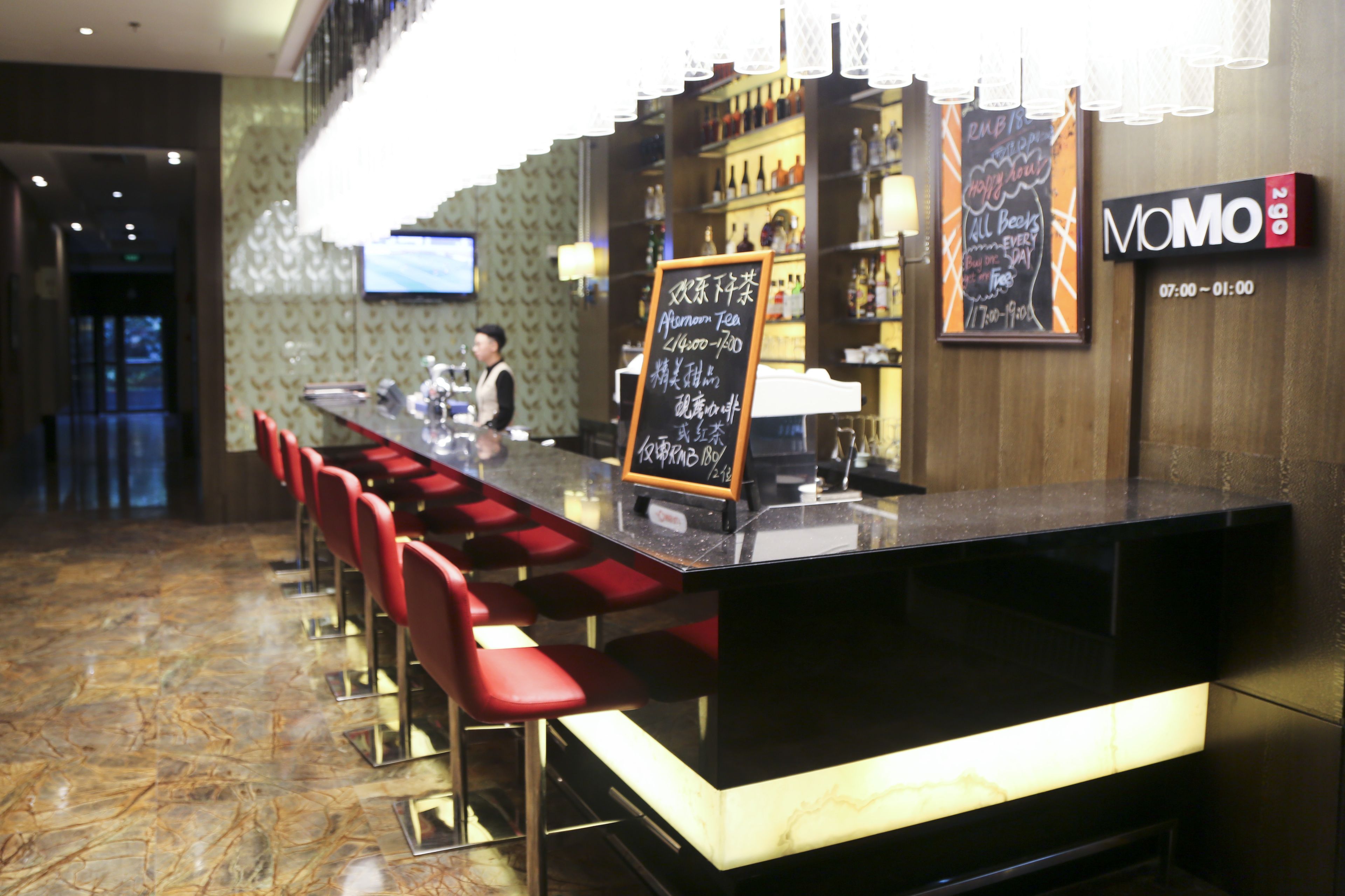 Un área de bar con una barra negra, taburetes rojos y un menú en una pizarra.