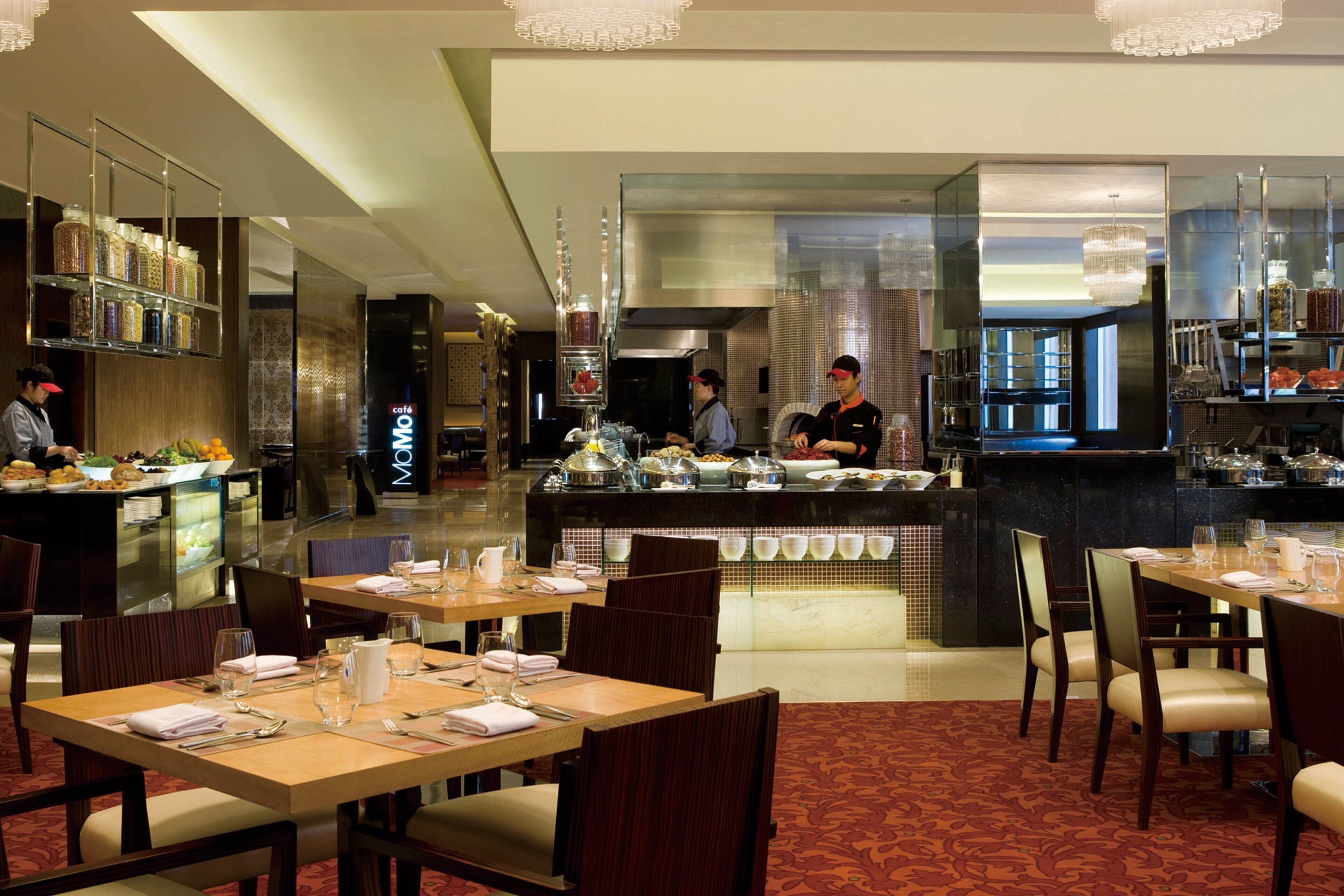 A restaurant with multiple dining tables, a buffet area, and a kitchen in the background.