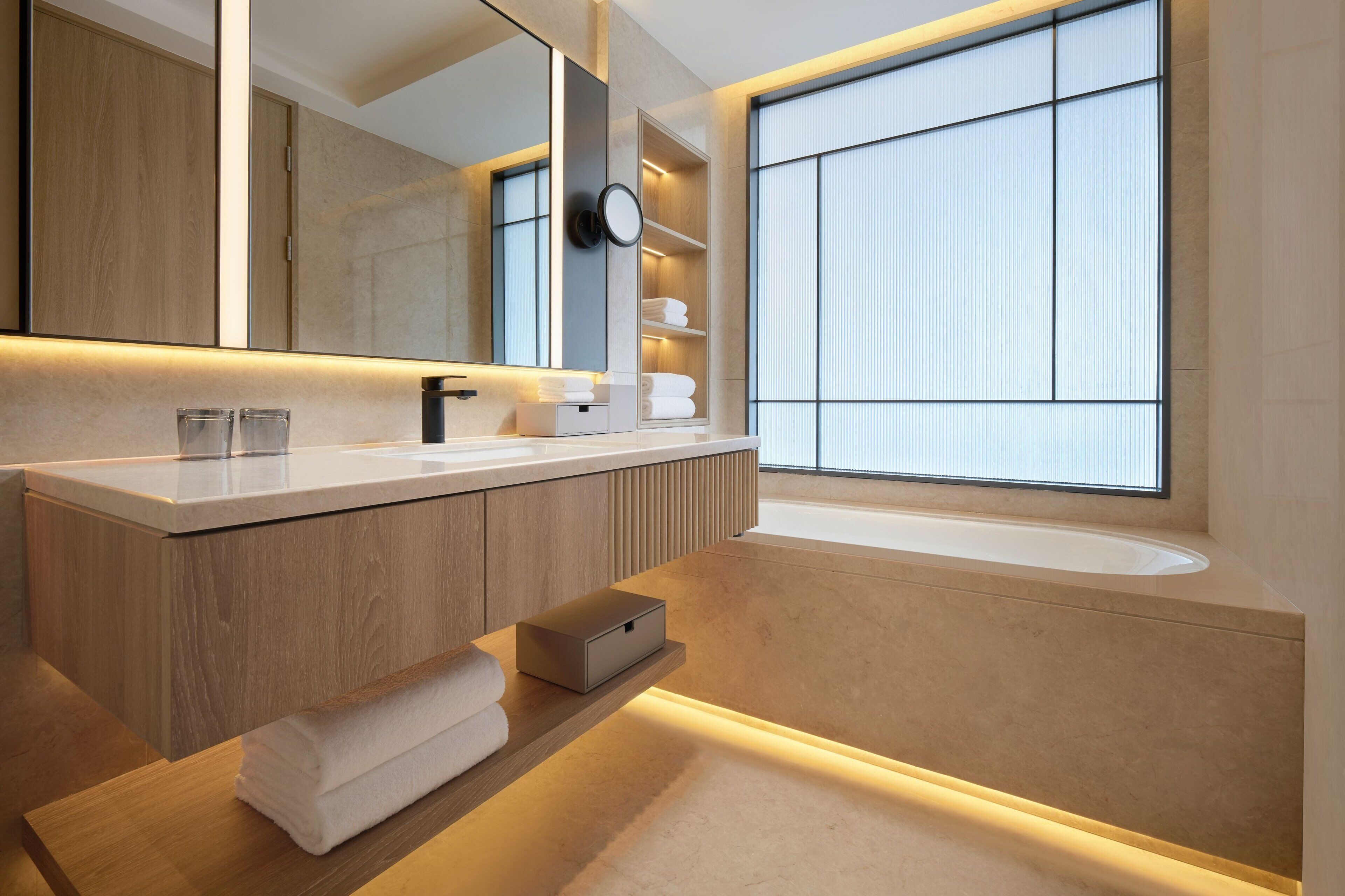 Une salle de bain moderne avec un grand miroir, des meubles en bois, une baignoire intégrée et une étagère avec des serviettes.