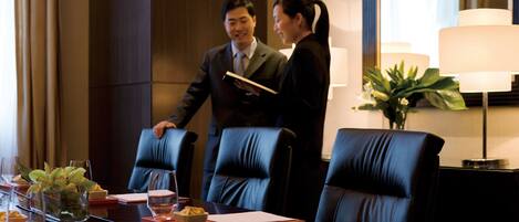 Un salón de conferencias con una mesa de madera oscura, sillas de cuero y un ventanal con cortinas.