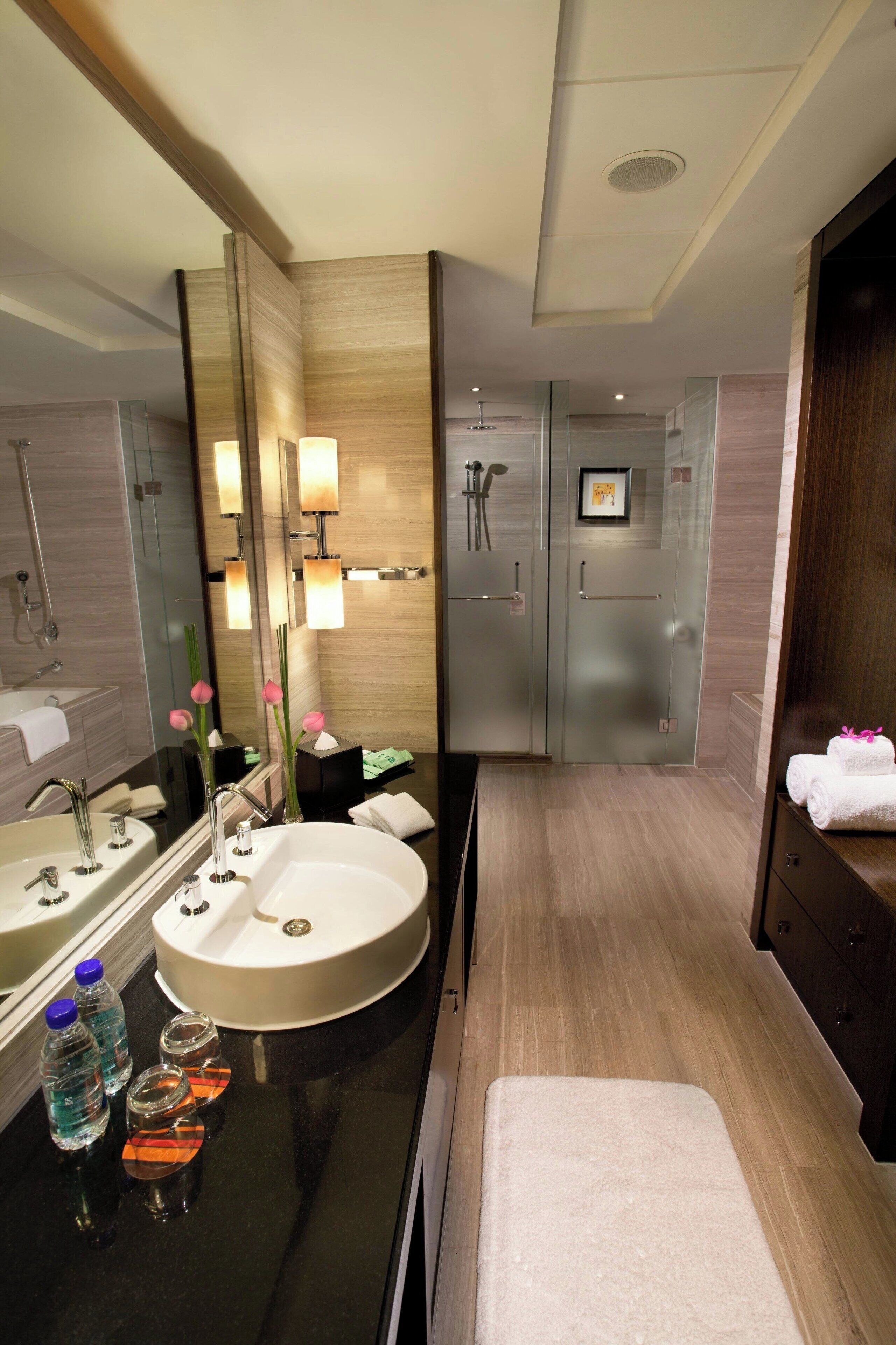 A modern bathroom with a large mirror, two sinks, a shower area, and a vanity with a towel rack.