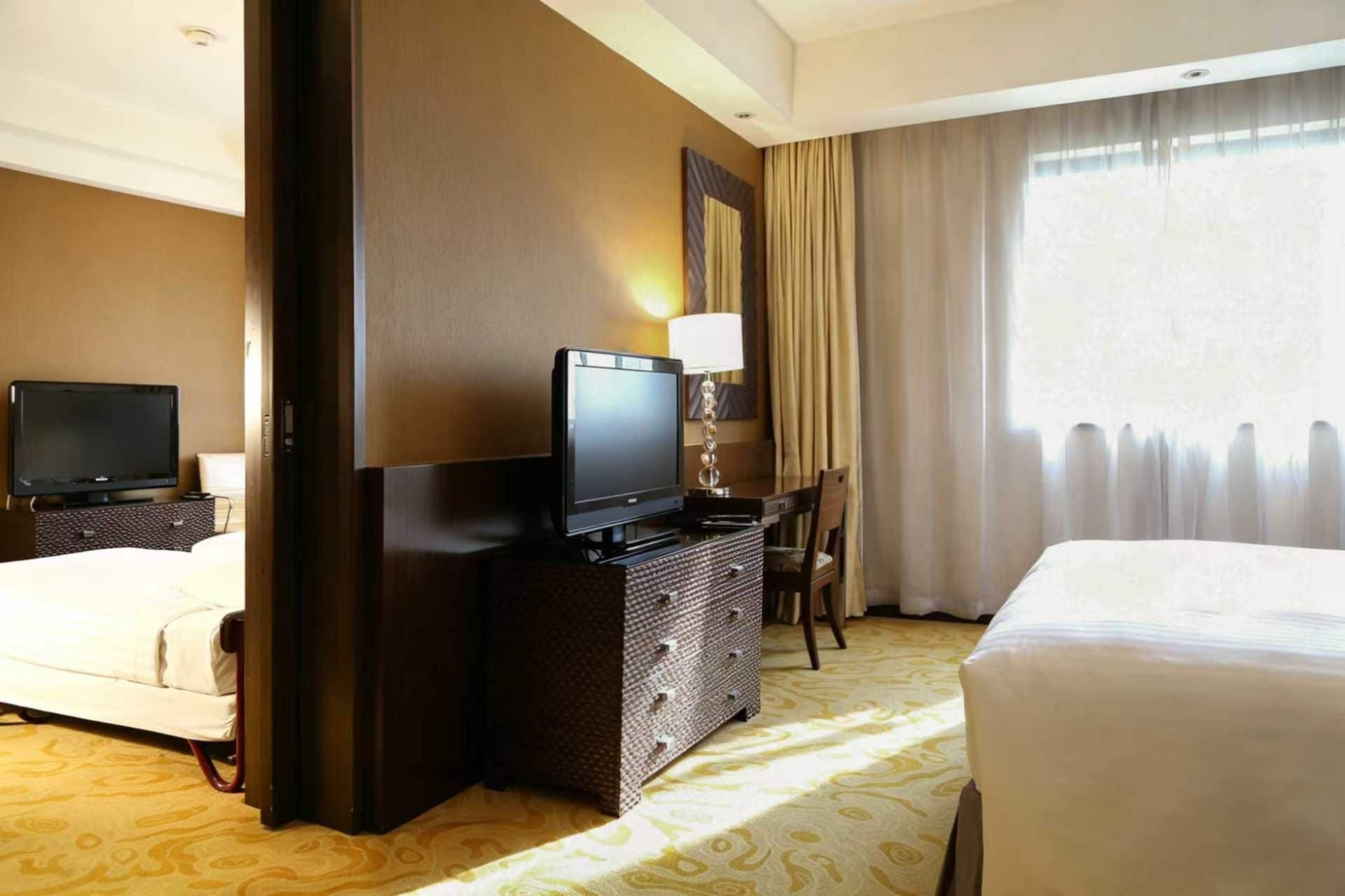 A hotel room with a bed, a TV, a dresser, and a window with curtains.
