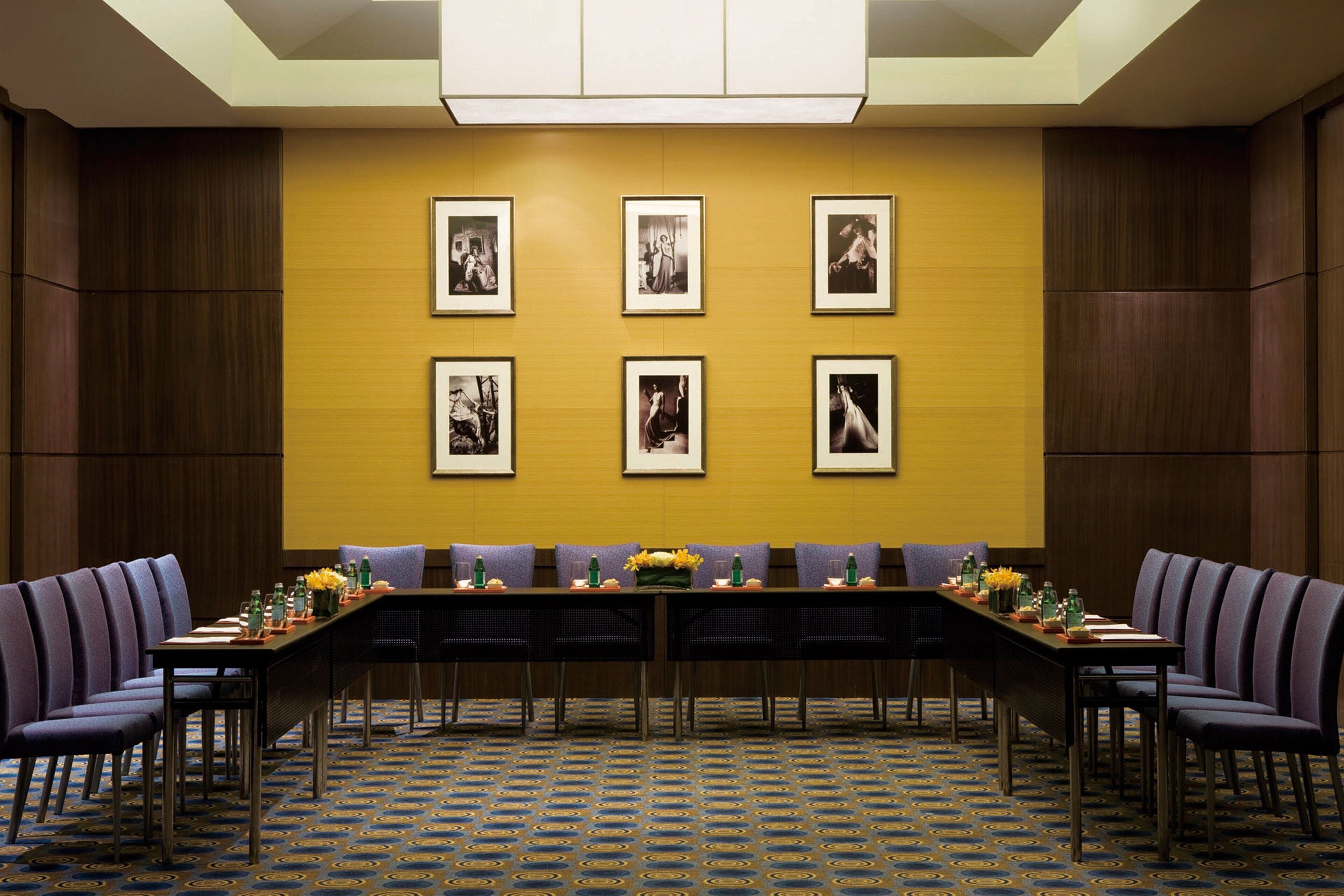 A conference room with a long table, chairs, framed pictures on the wall, and a patterned carpet.