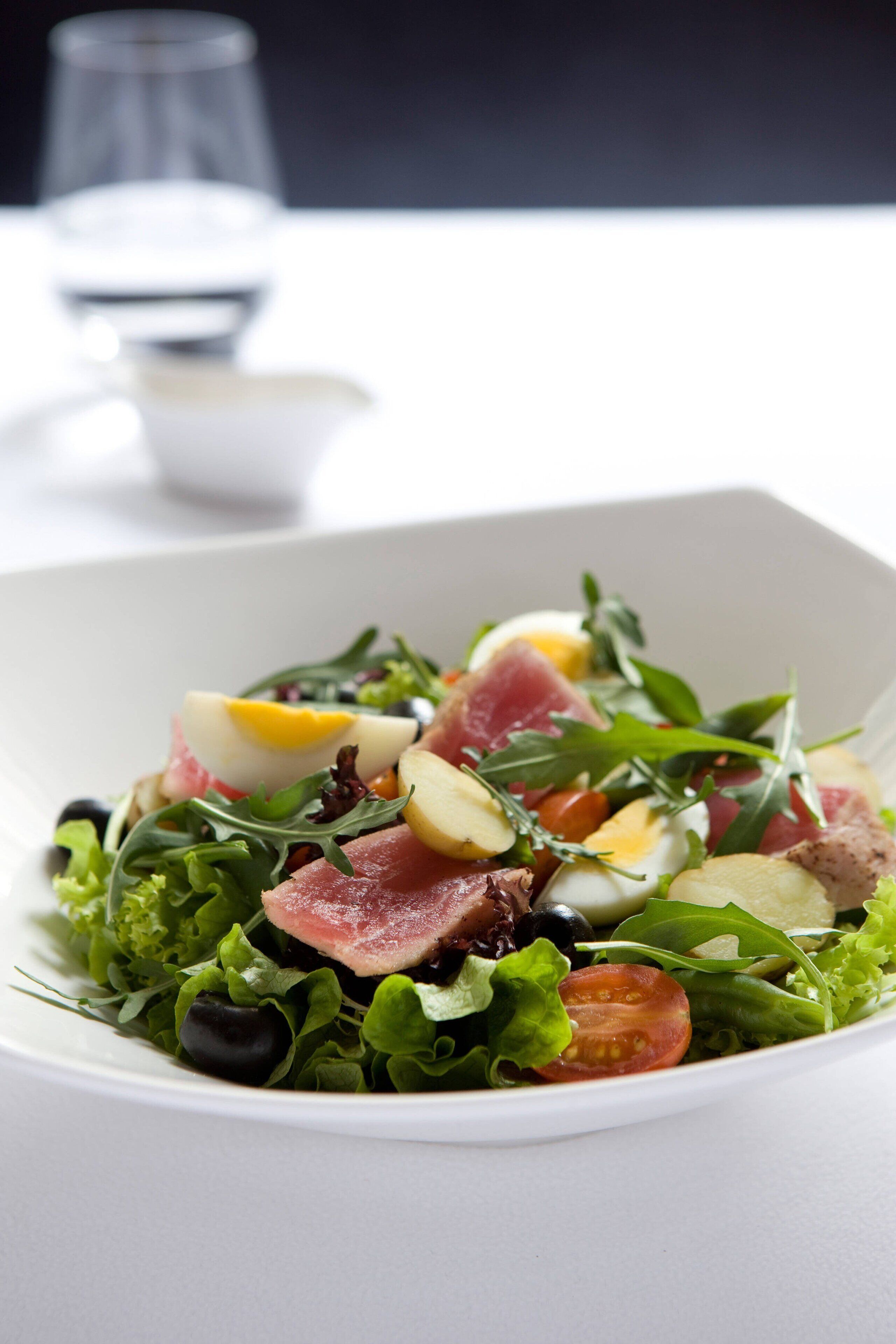 Un tazón blanco con ensalada de hojas verdes, tomates, huevos y carne.