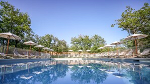 Una piscina con sillas de descanso y sombrillas, rodeada de árboles.