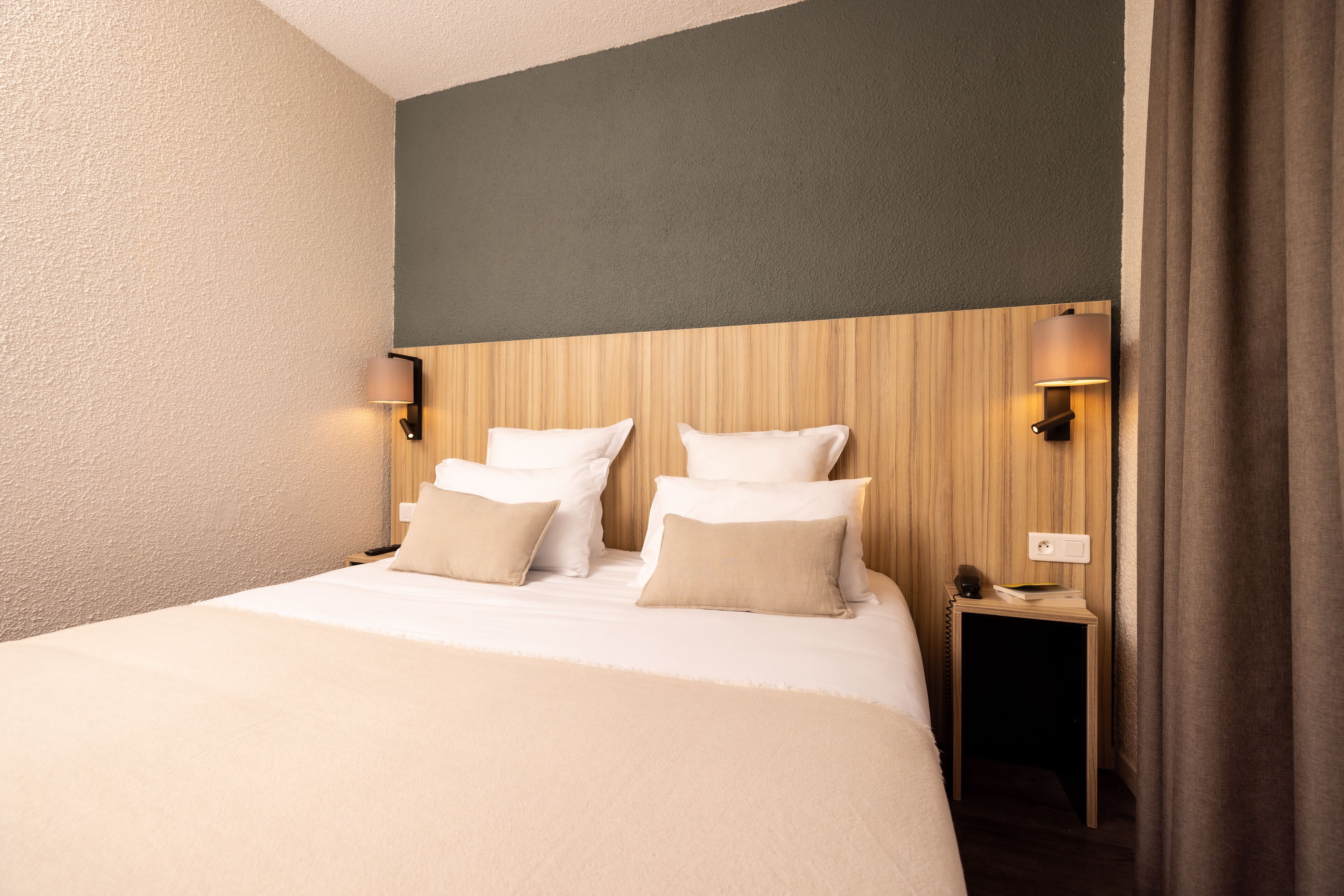 A hotel room with a large bed, two bedside lamps, a wooden headboard, and a nightstand with a lamp.
