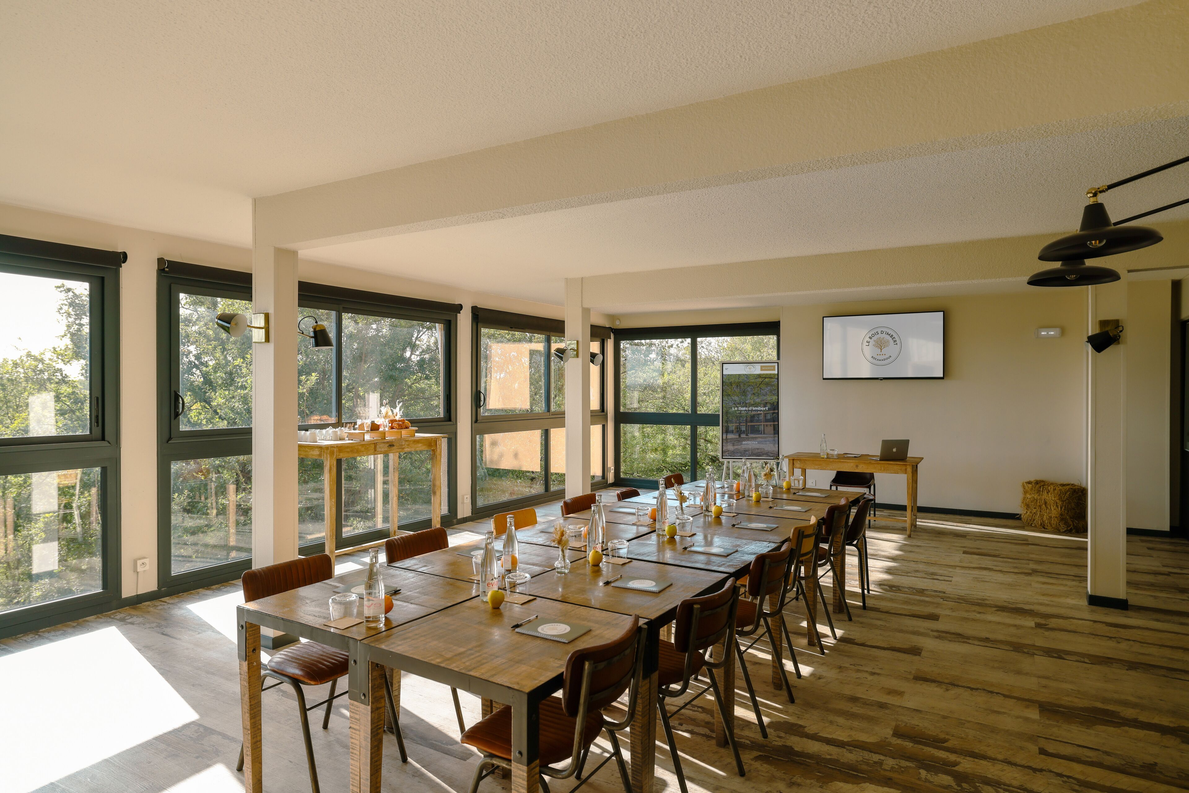 A conference room with a long table set for a meeting, large windows, and a projector screen on the wall.