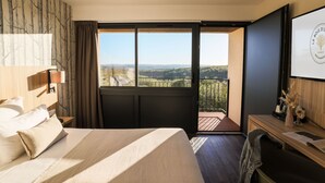 Habitación de hotel con una cama grande, un escritorio, una silla, un televisor y un balcón con vistas al campo.