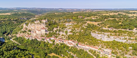 An aerial view of a historic town with a prominent castle, narrow winding roads, and surrounding greenery.