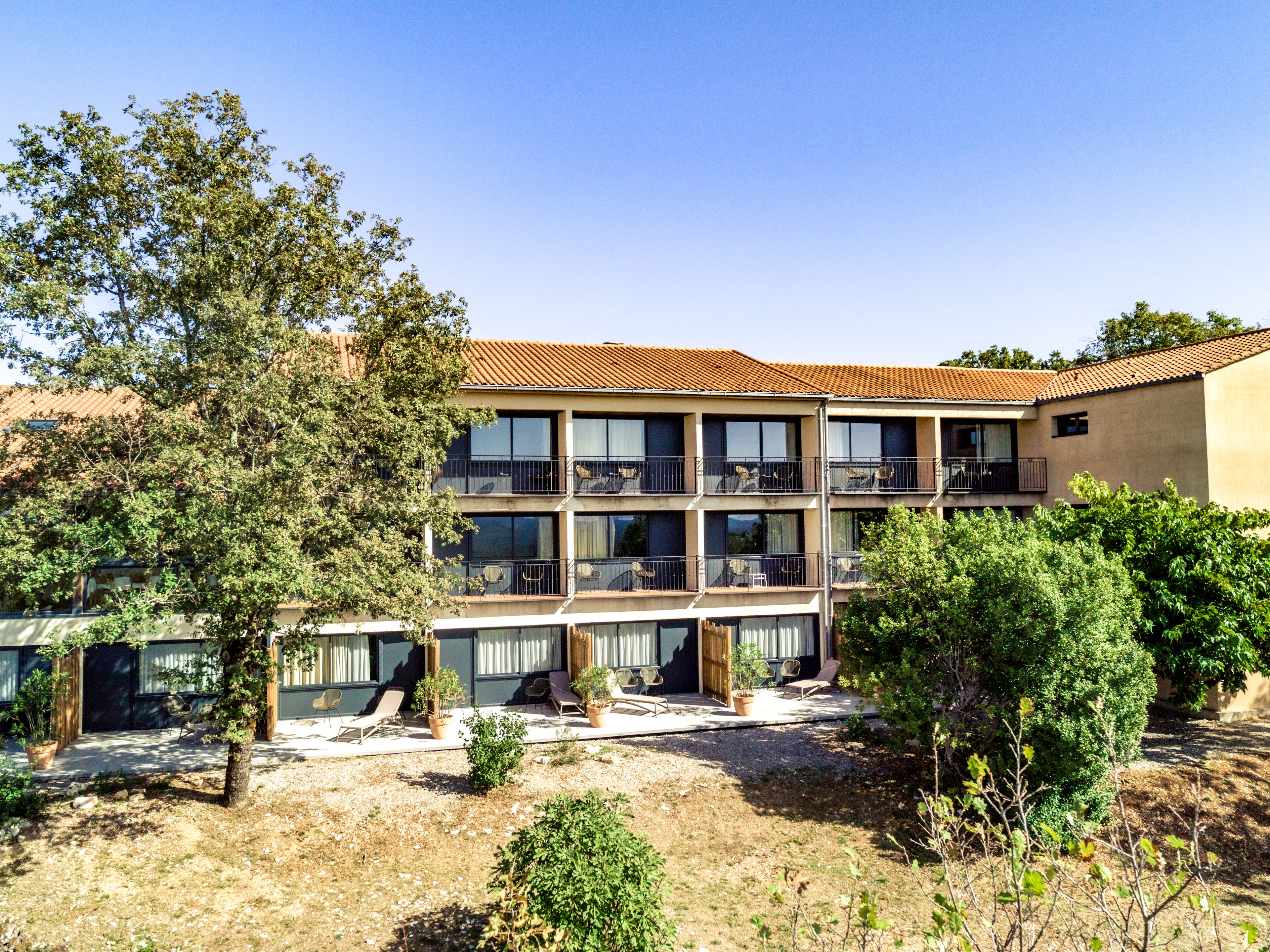 A multi-story building with balconies, a courtyard with seating, and surrounding greenery.