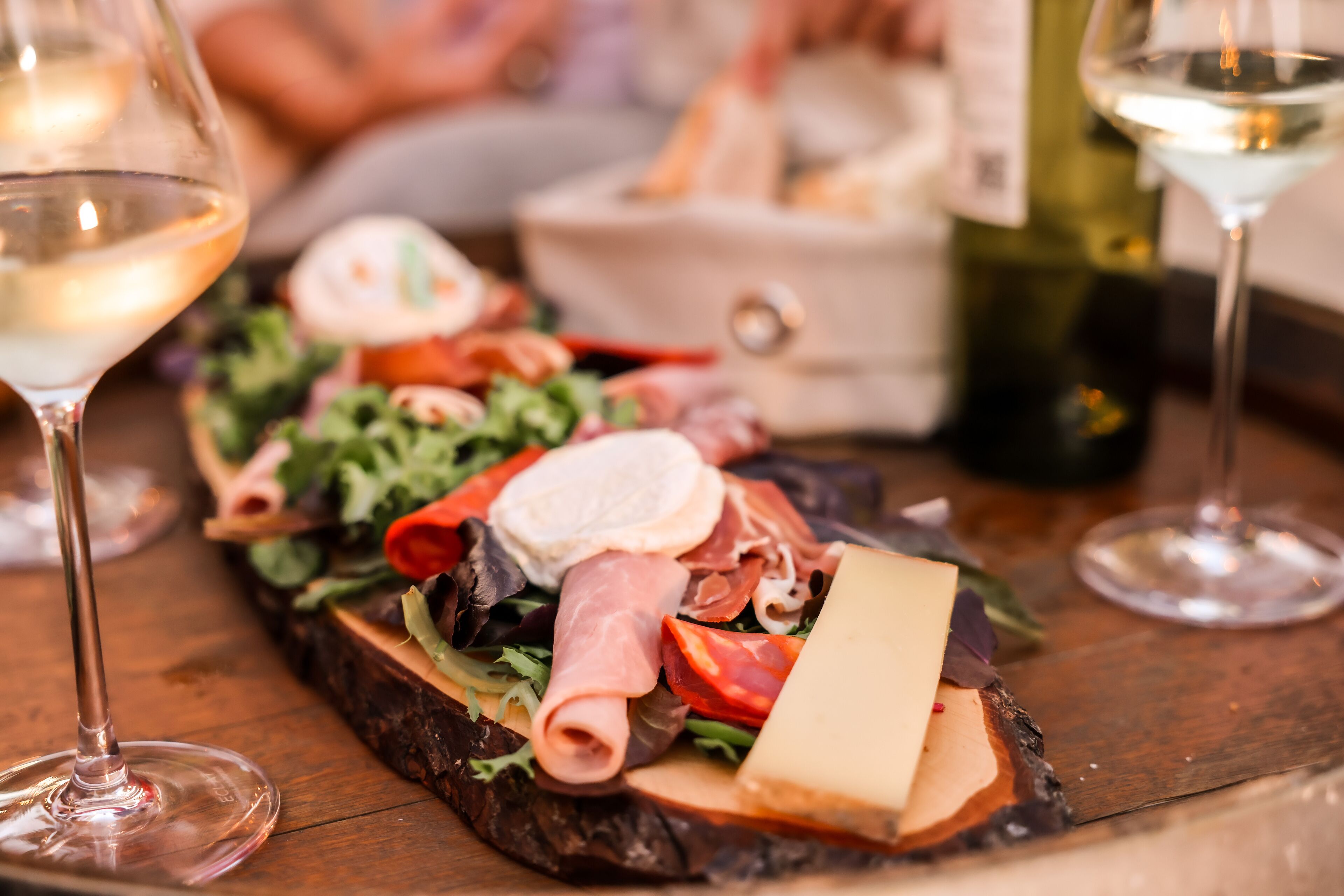 Una tabla de embutidos con diversos tipos de carne, quesos y verduras, acompañada de copas de vino.
