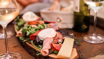 Una tabla de embutidos con diversos tipos de carne, quesos y verduras, acompañada de copas de vino.