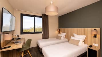 A hotel room with two beds, a desk with a laptop, a chair, a TV, and a window with a view.