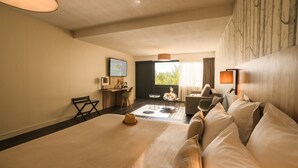 Habitación de hotel con una cama grande, un sofá, un escritorio y una silla. Cuenta con una ventana con cortinas y vistas a árboles.