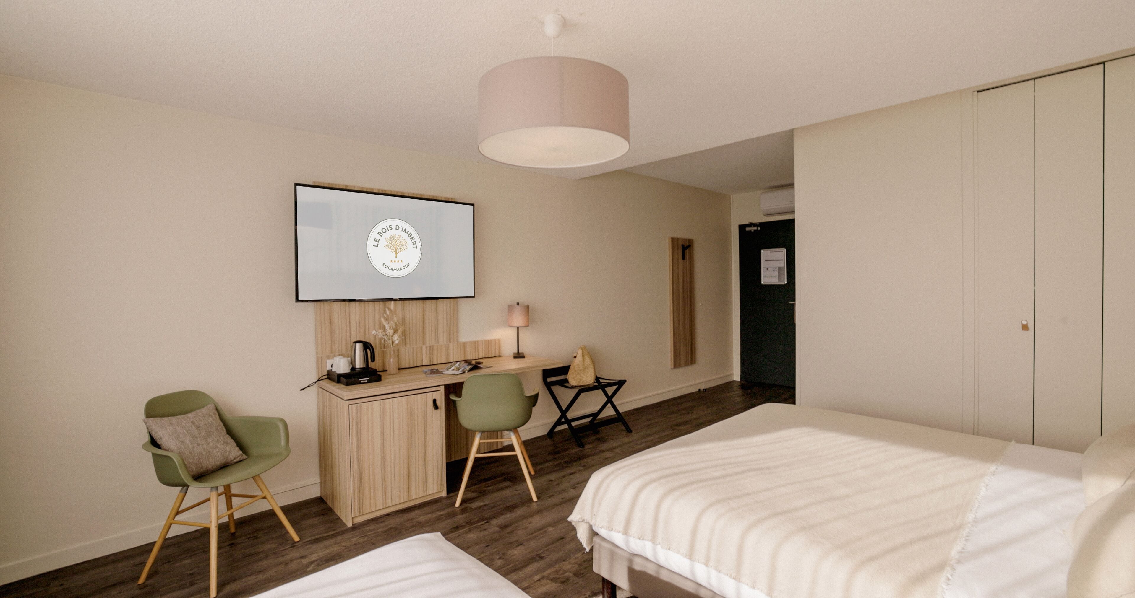 Habitación de hotel con cama, escritorio con computadora, silla y televisor en la pared.