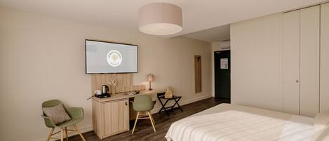 A hotel room with a bed, a desk with a computer, a chair, and a television mounted on the wall.